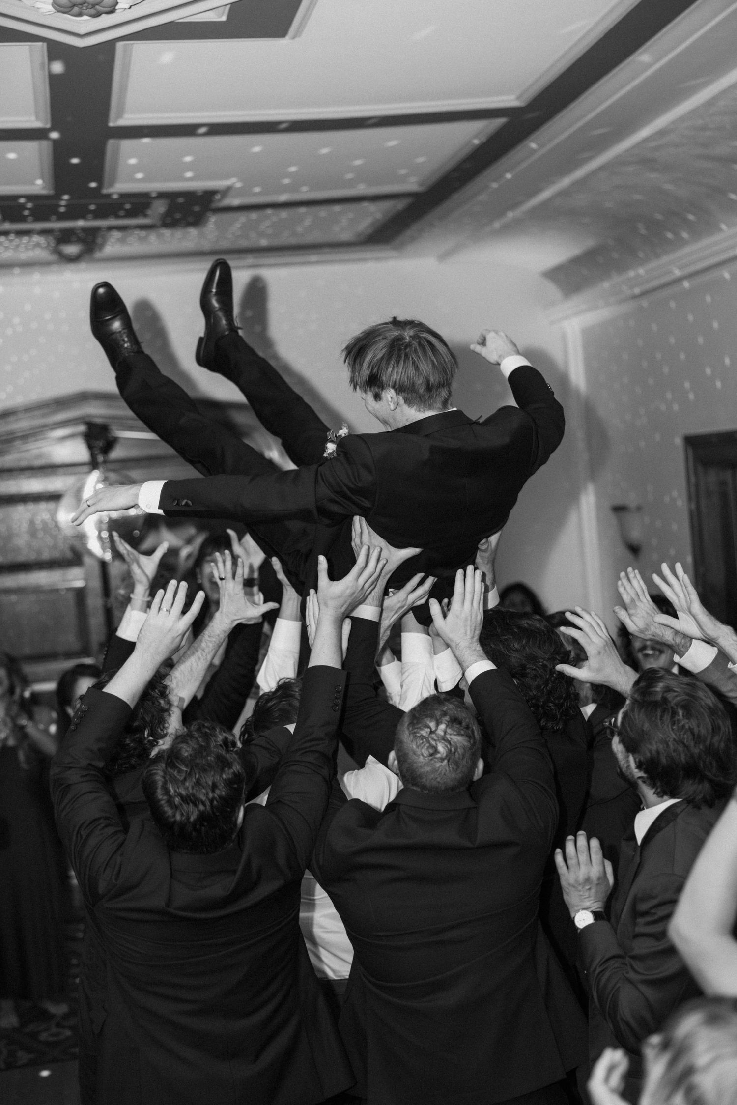 Wedding guests with raised hands dancing in celebration at an indoor reception.