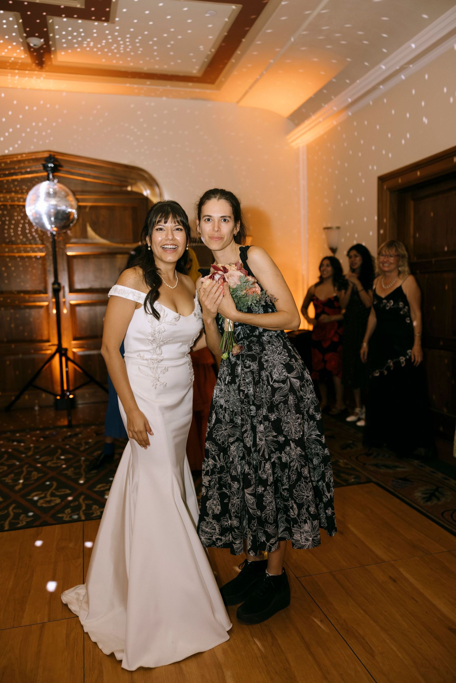 People dancing on a wooden dance floor under twinkling lights at an indoor event.
