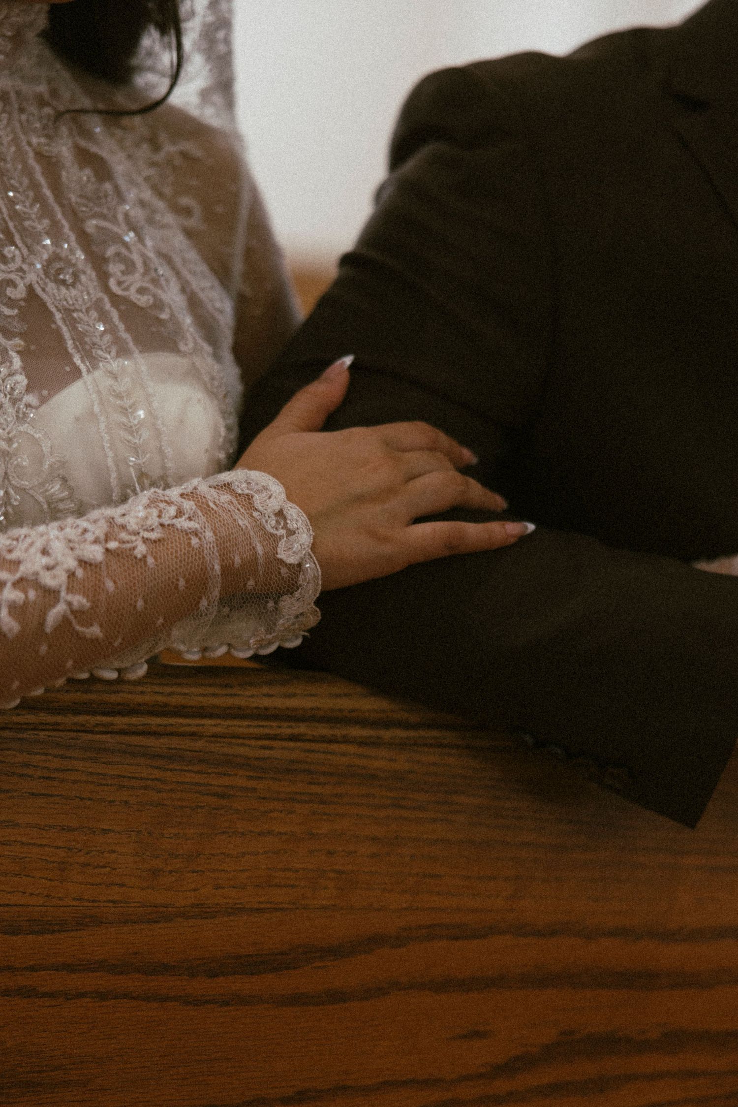 A close-up of lace sleeve and hands resting on a wooden church pew.