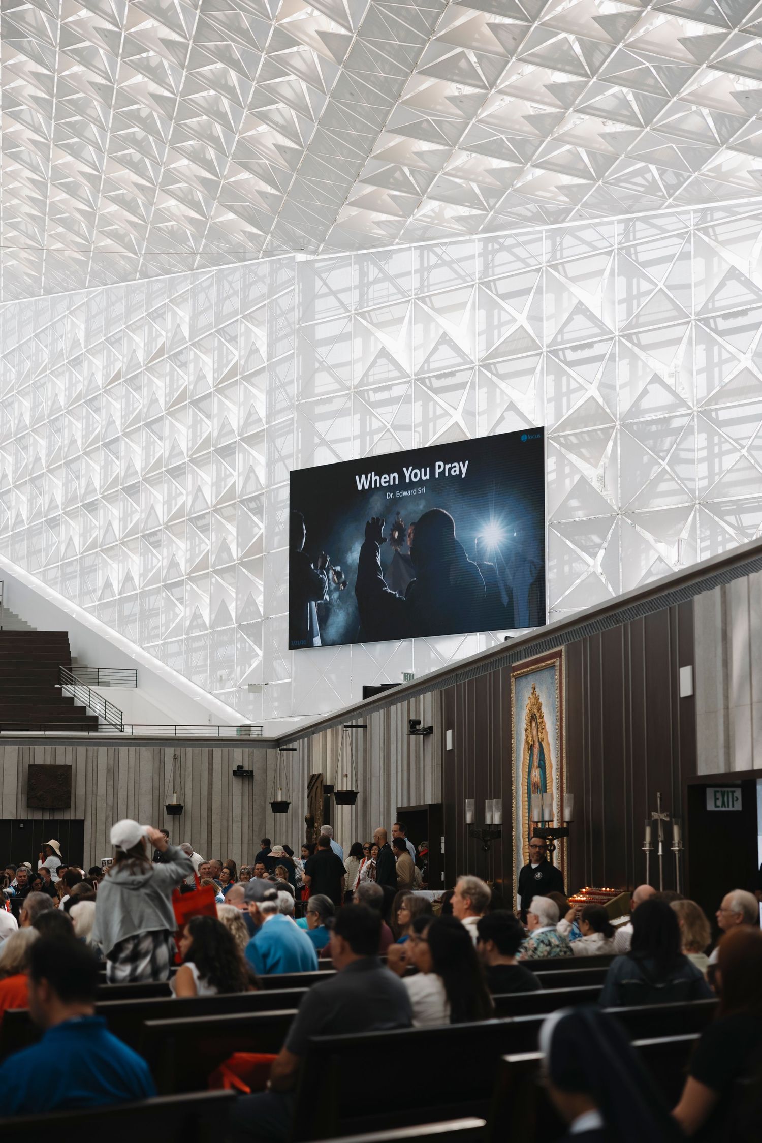 Audience watches movie screening in auditorium with geometric ceiling pattern.