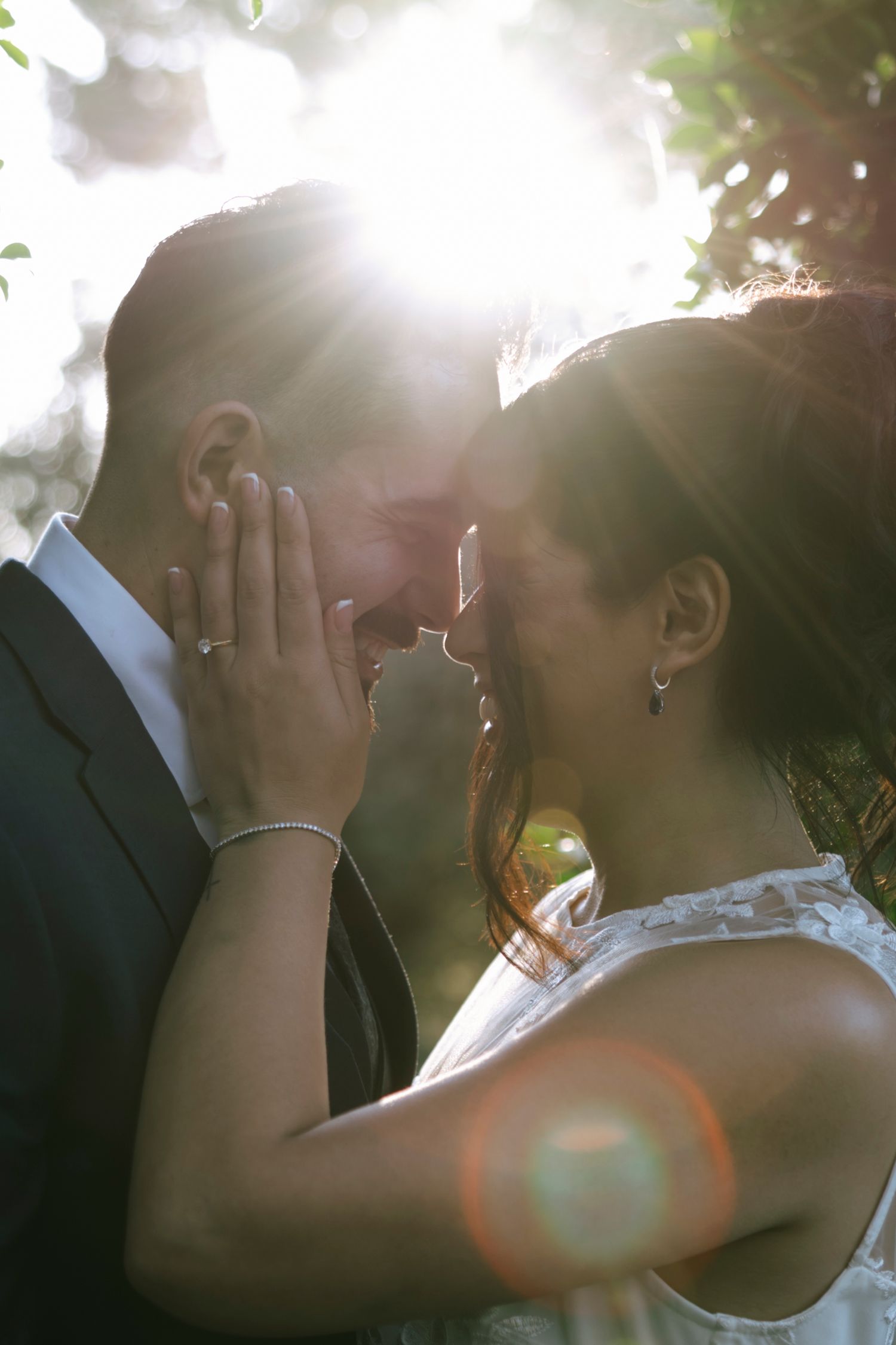 Romantic sunlit portrait of couple embracing outdoors during wedding photoshoot.