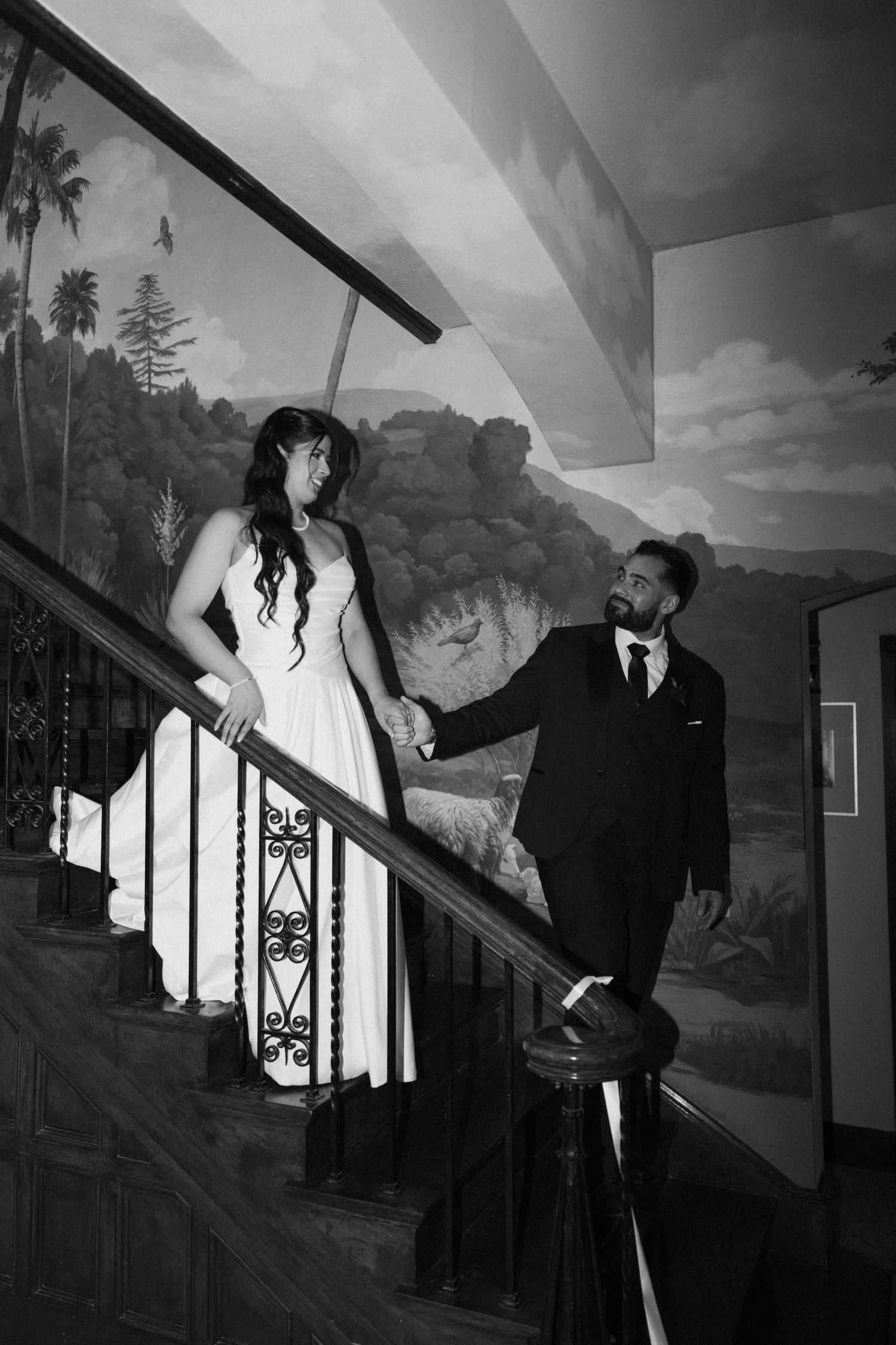Black and white romantic portraits on vintage staircase with painted scenery.