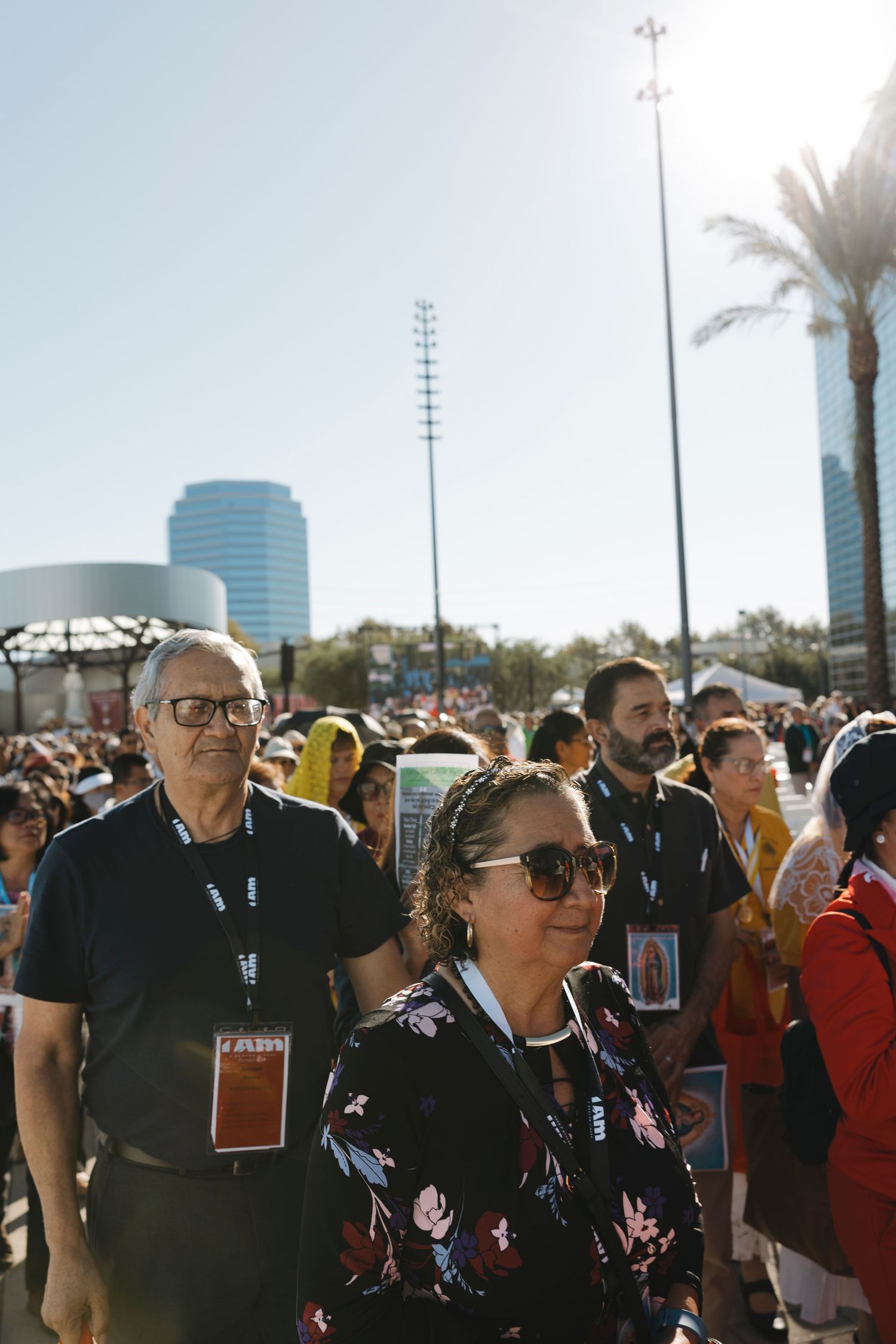 Crowd gathered outside modern building for religious event with palm trees in background.