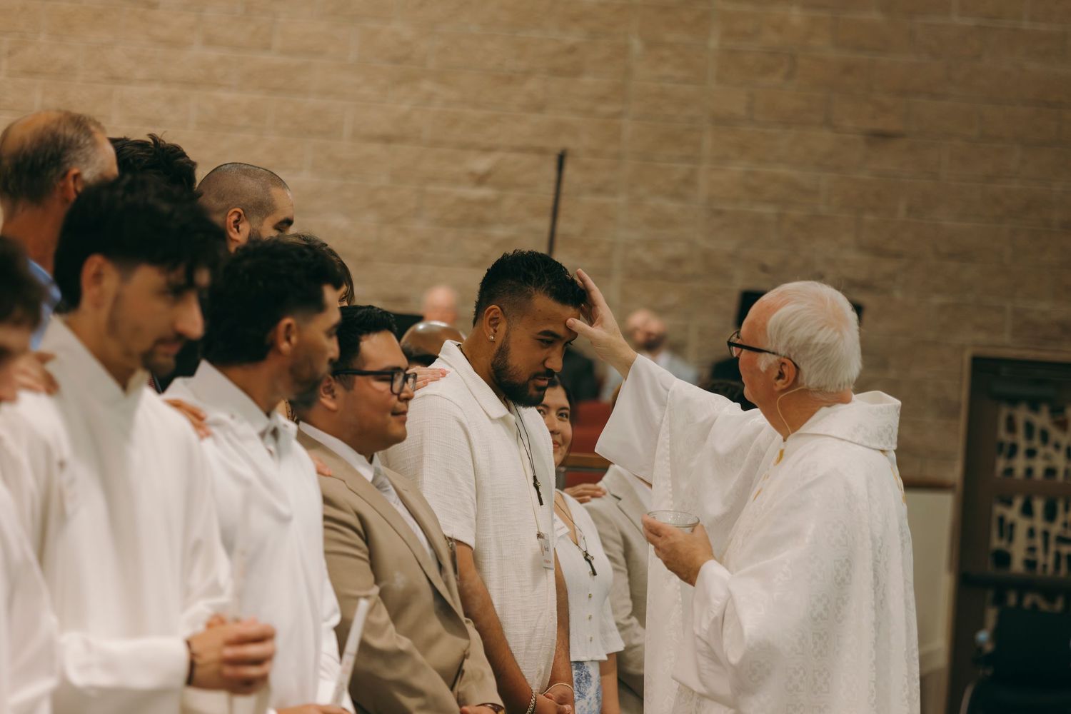 Religious ceremony with robed clergy blessing young men in white attire inside a stone church.