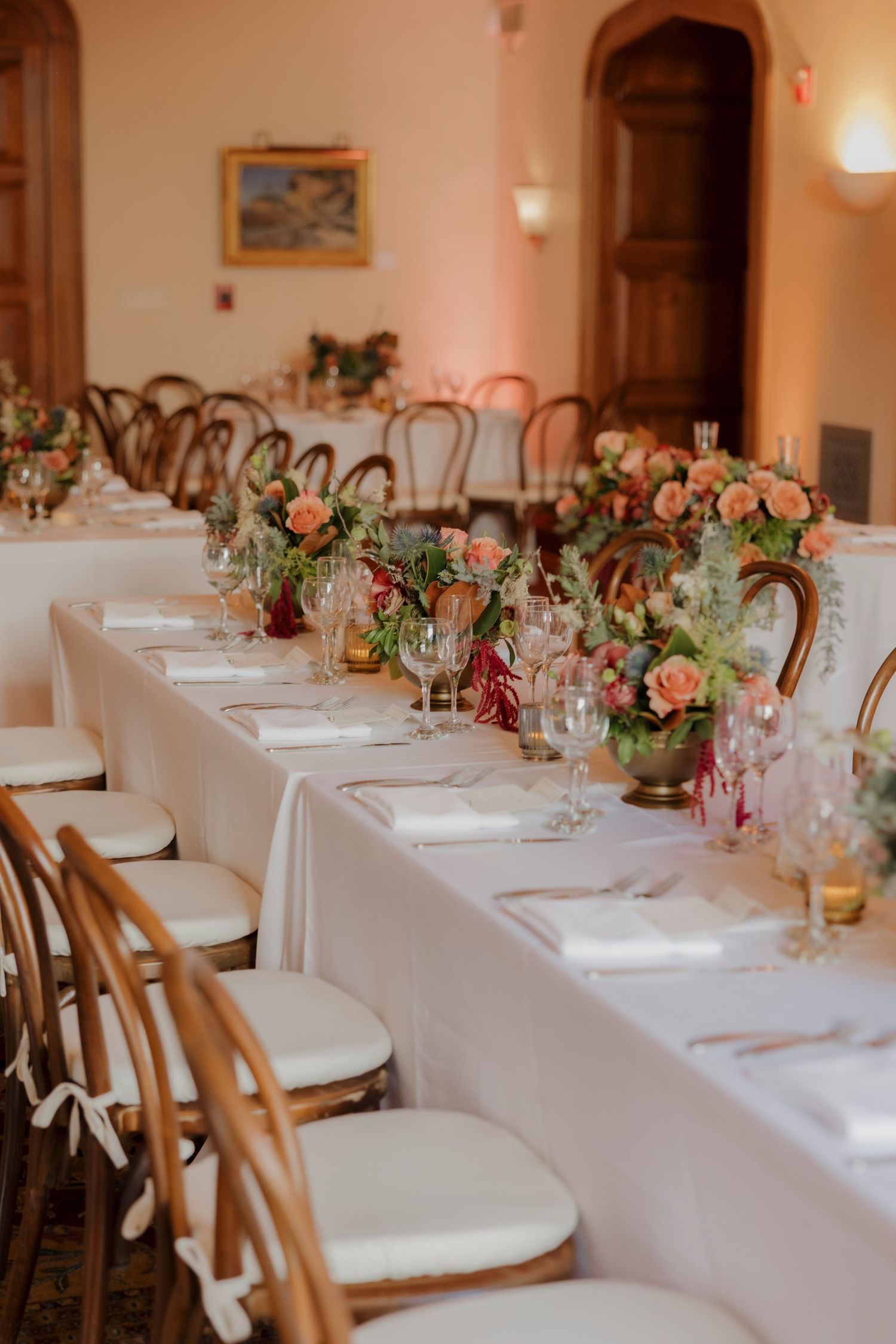 Wedding reception dining room with long tables, bentwood chairs and romantic floral arrangements.