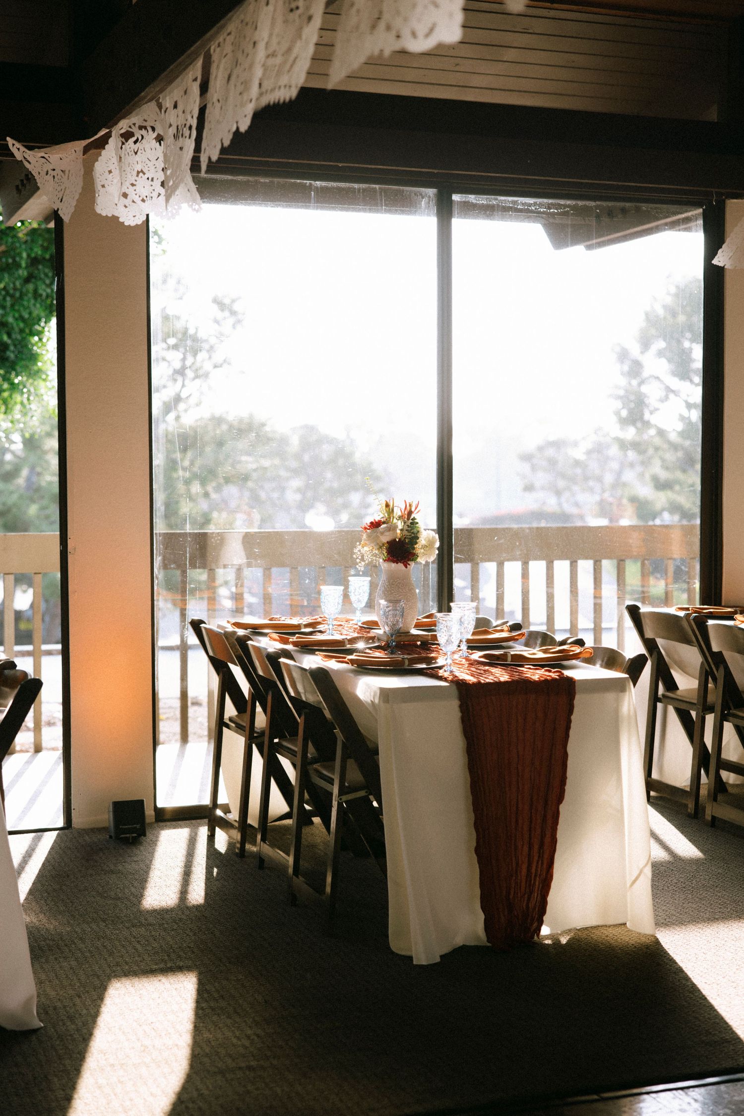 Spacious reception venue with white-covered chairs and large windows overlooking scenic outdoor views.