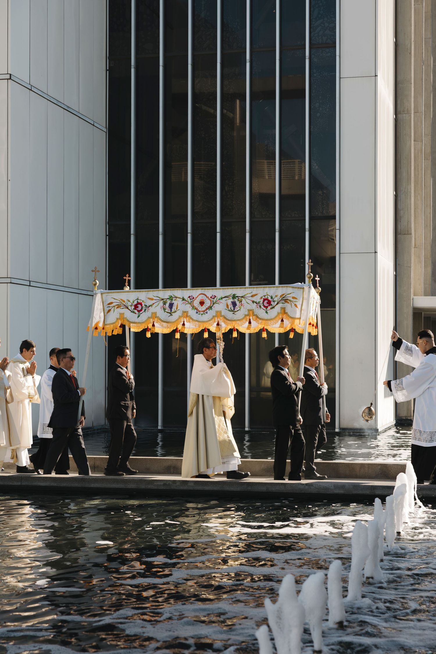 Religious ceremony taking place around a reflecting pool with white columns and formal attire.