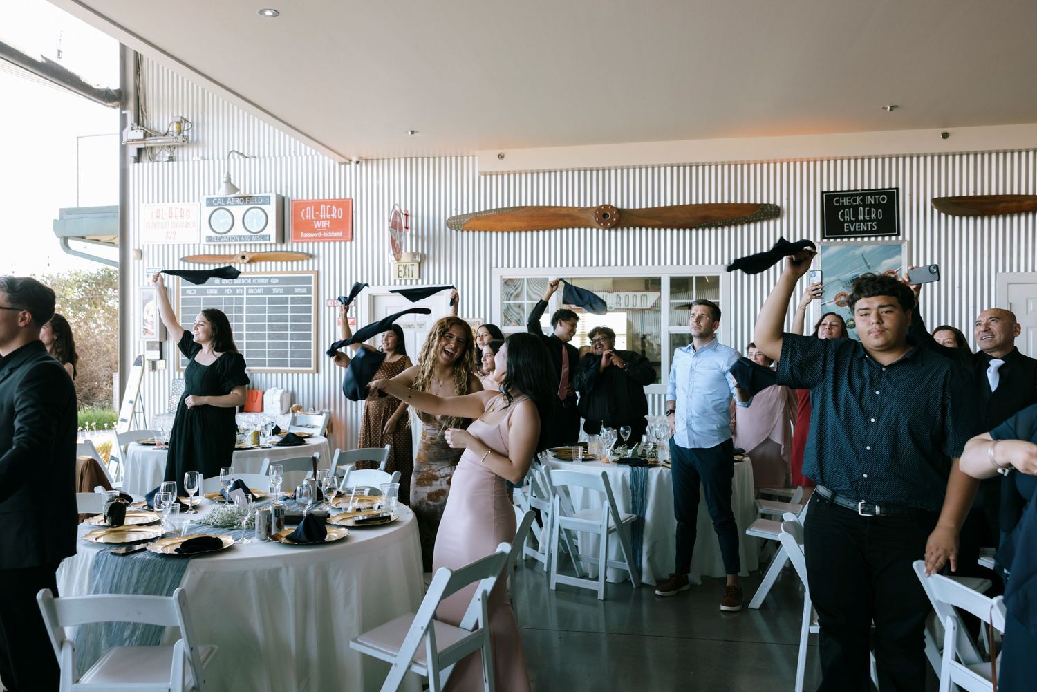 Indoor wedding reception venue with guests mingling among decorated tables and chairs.