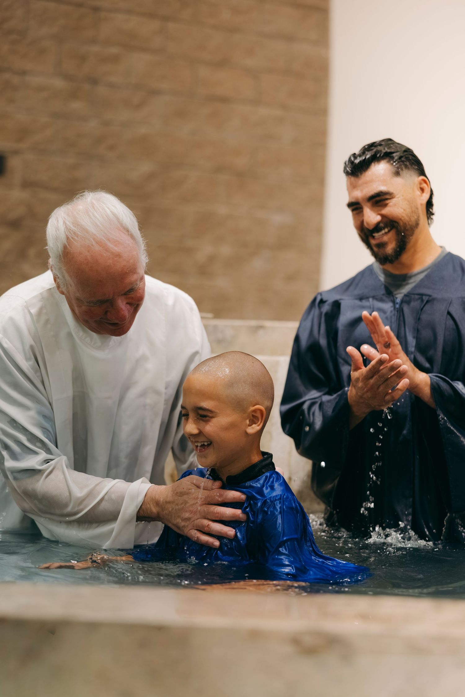 Elderly pastor baptizing a smiling young boy in a baptismal pool during a church service.