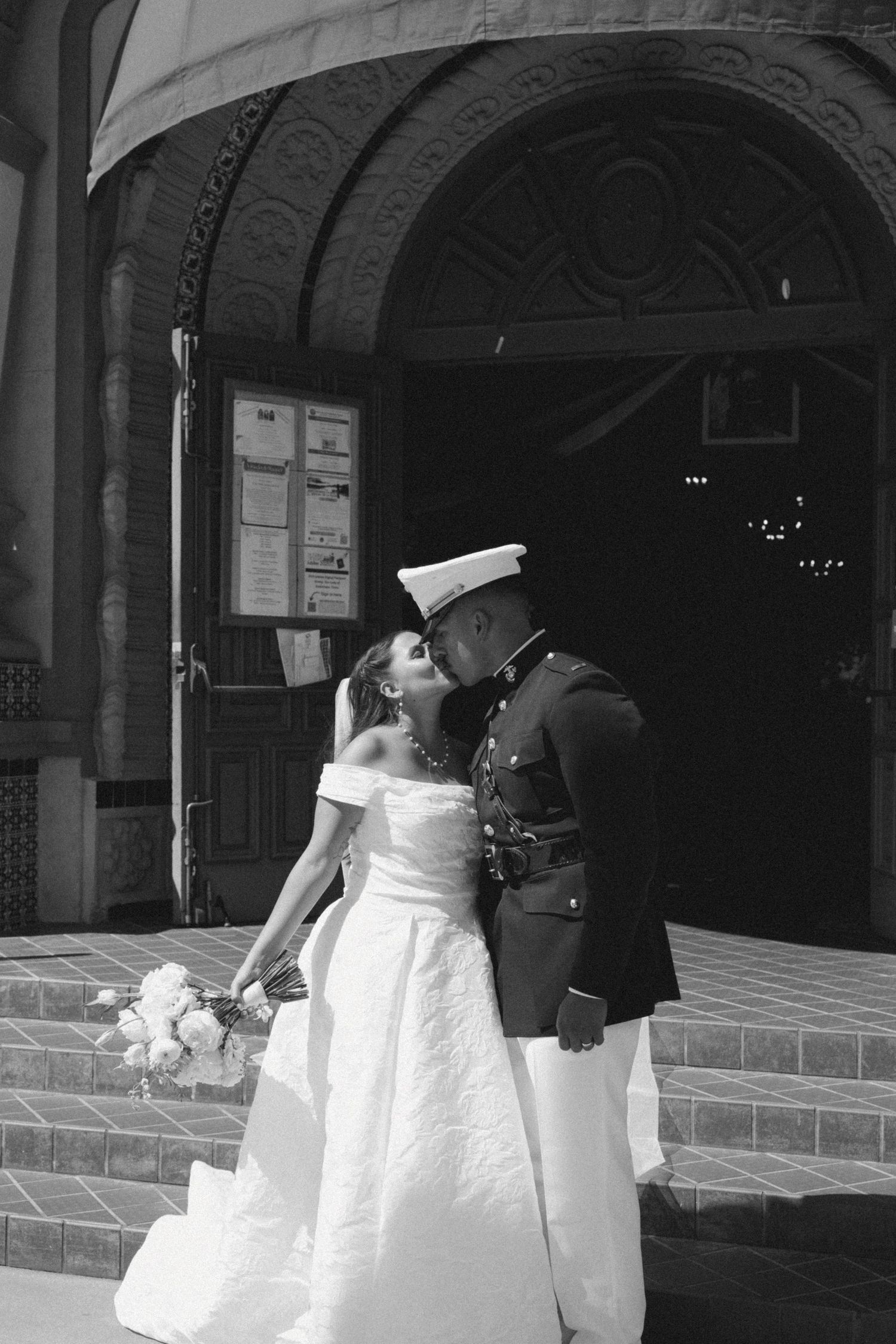 Bridesmaids in white dresses gather under an ornate archway entrance.
