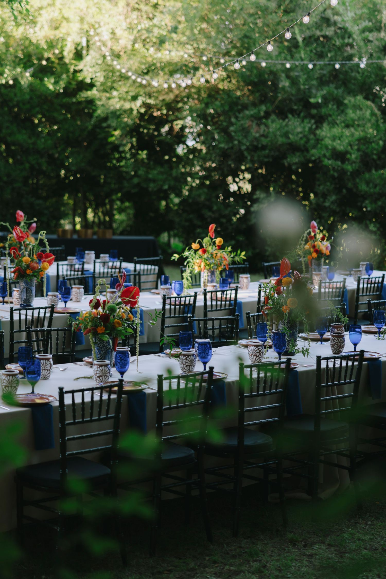 Elegant outdoor dining setup with black chairs and vibrant floral arrangements on white tablecloths.