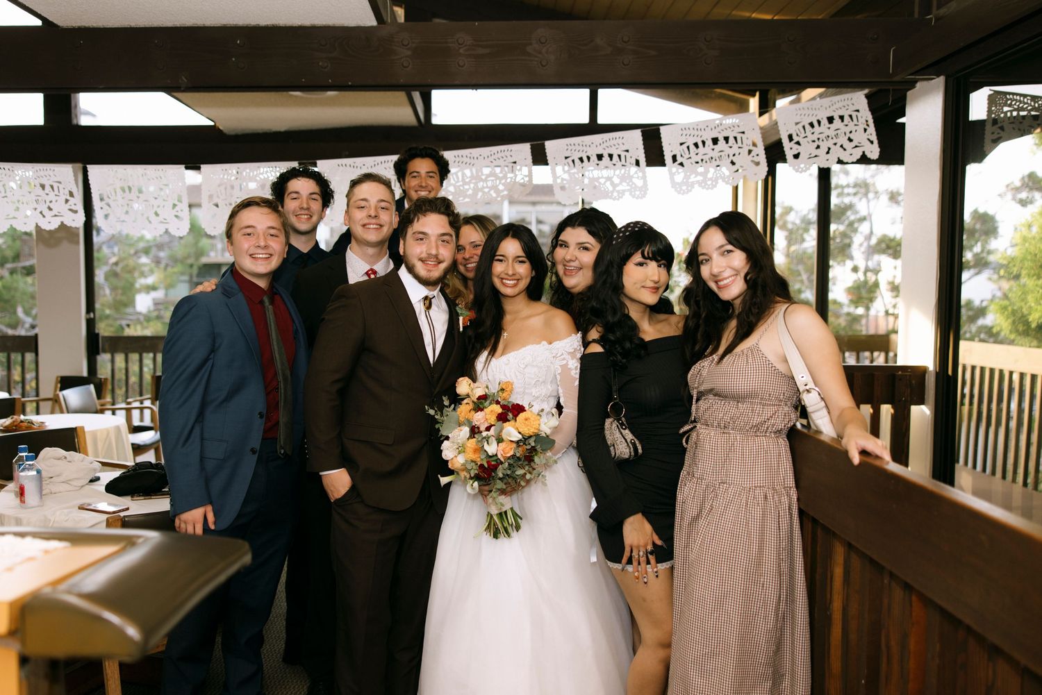 Wedding party gathered for group photos in a rustic venue with natural lighting.
