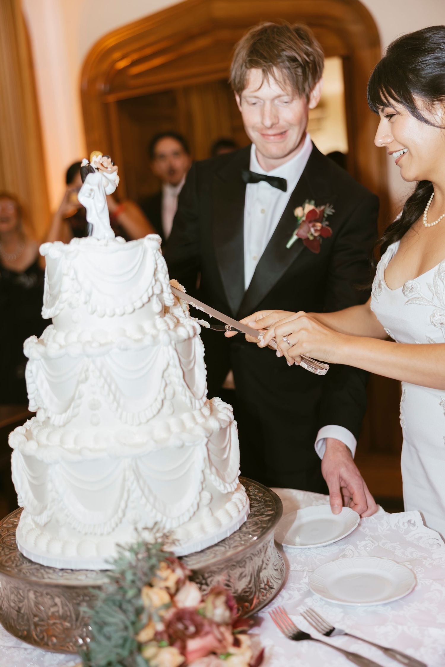 Traditional white tiered wedding cake being cut during reception celebration.
