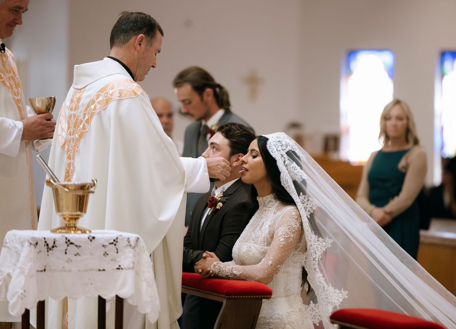 Catholic wedding ceremony with bride in lace veil and clergy at altar.