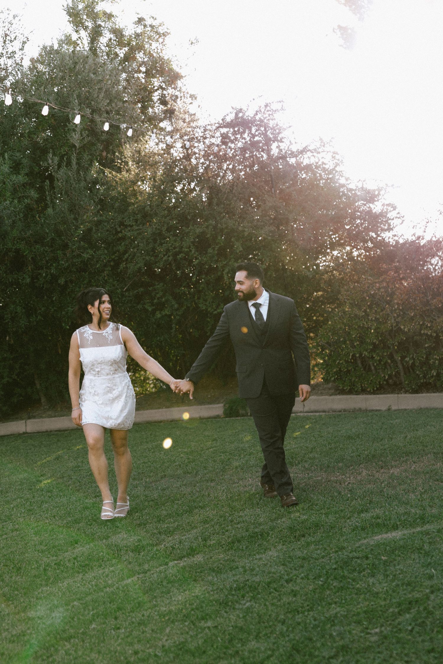 Couple playing and laughing together on grassy slope during sunset photoshoot.
