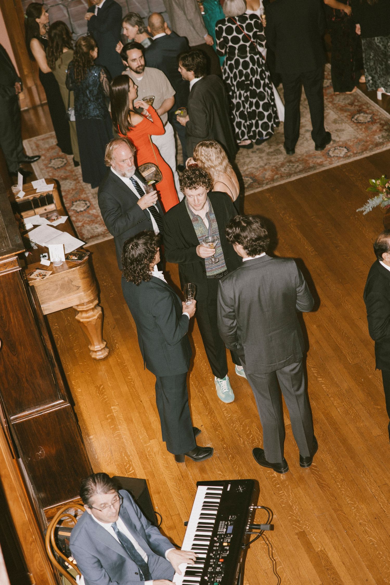 Wedding reception with guests mingling and pianist performing on hardwood floor.