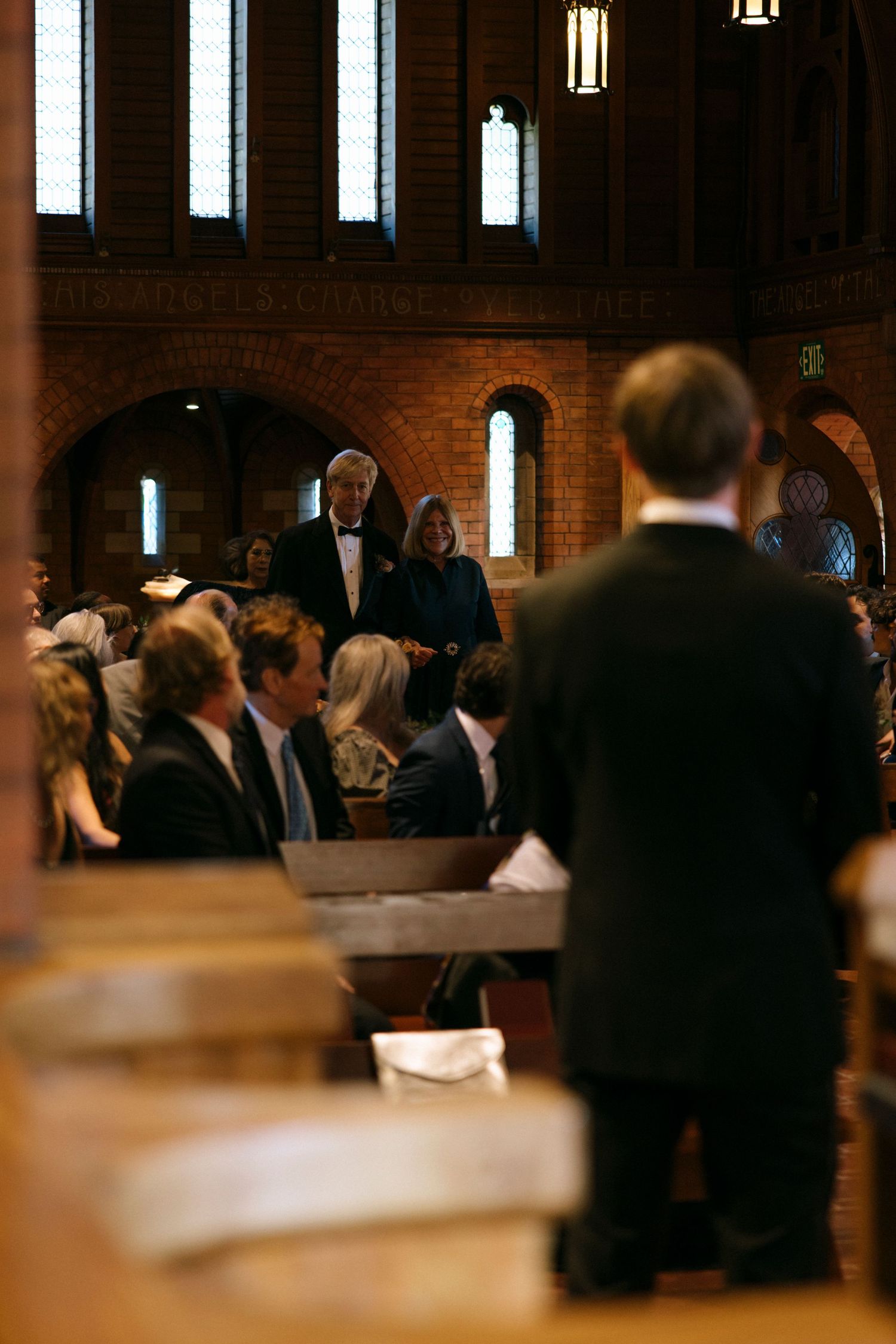 Wedding guests mingle in church reception area with warm lighting and brick walls.