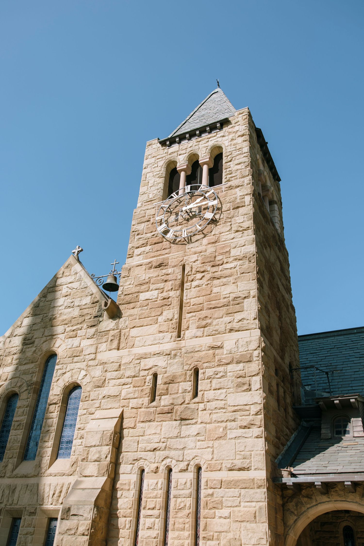 Stone church exterior with multiple towers and gothic architecture against bright blue sky.