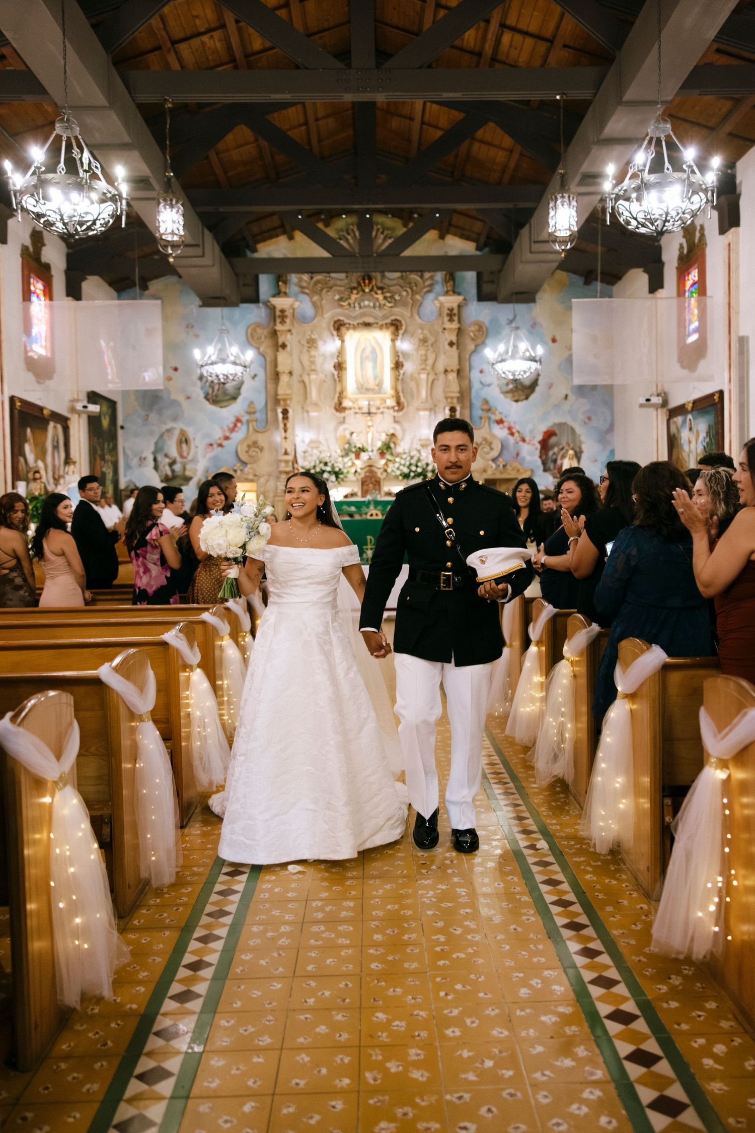 Wedding guests line the aisle of a grand church with chandeliers and wooden beams.