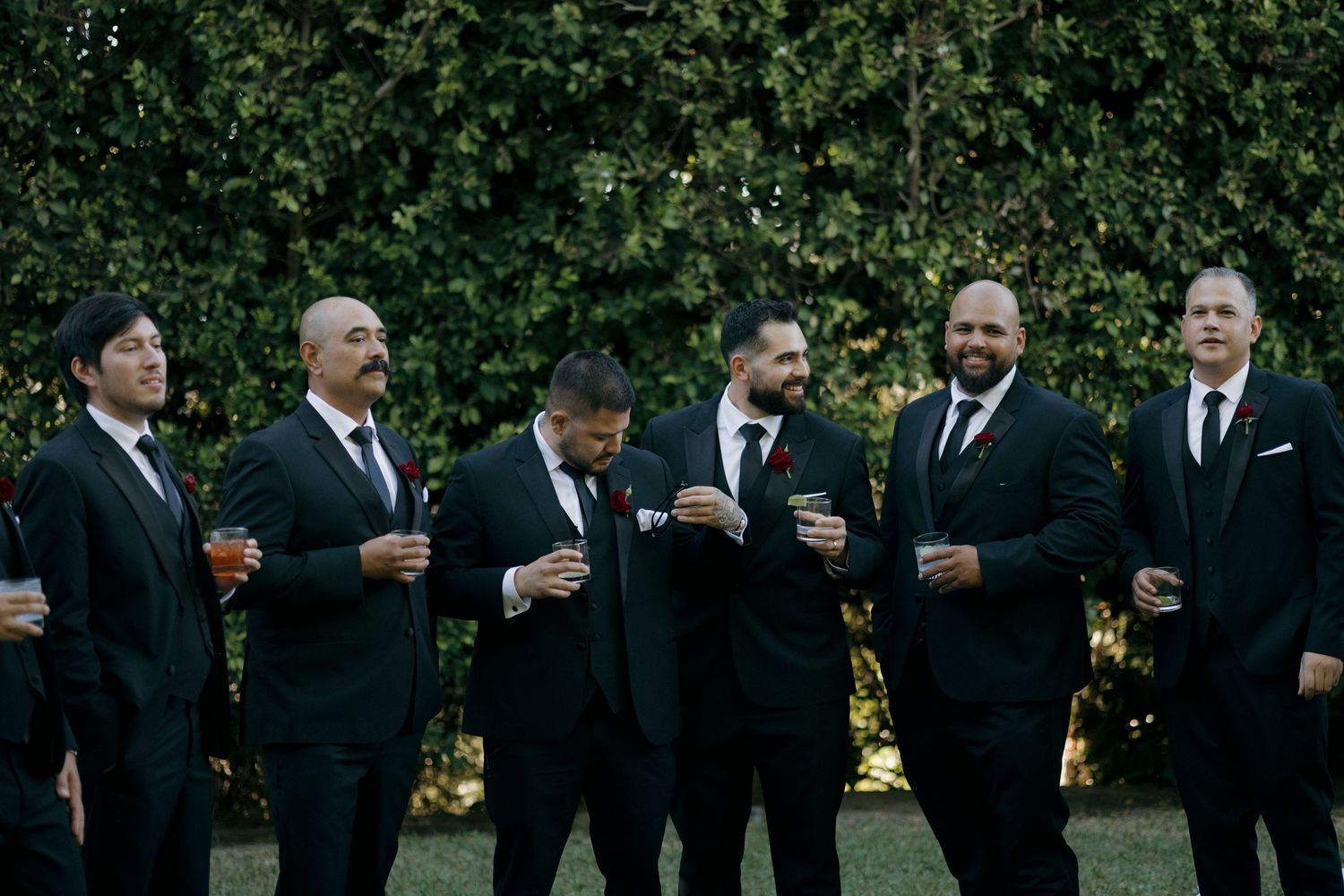 Groomsmen in black suits lined up outdoors for wedding photos.