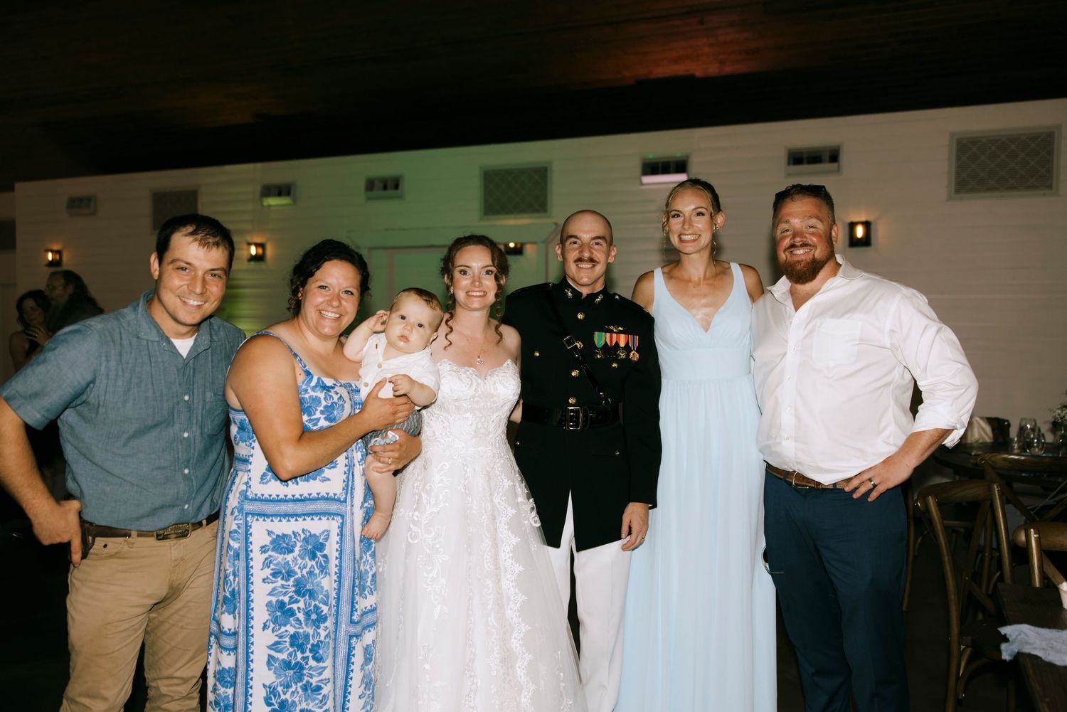 Military groom in dress uniform poses with bride and family members at wedding reception.