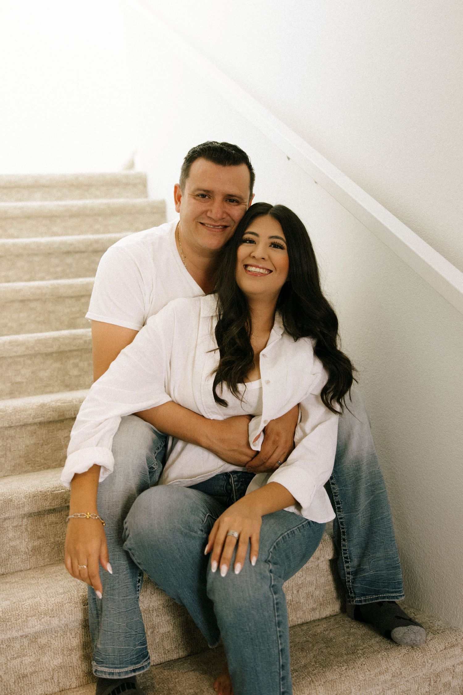 Couple in casual white shirts and jeans sitting together on stairs for an intimate portrait.