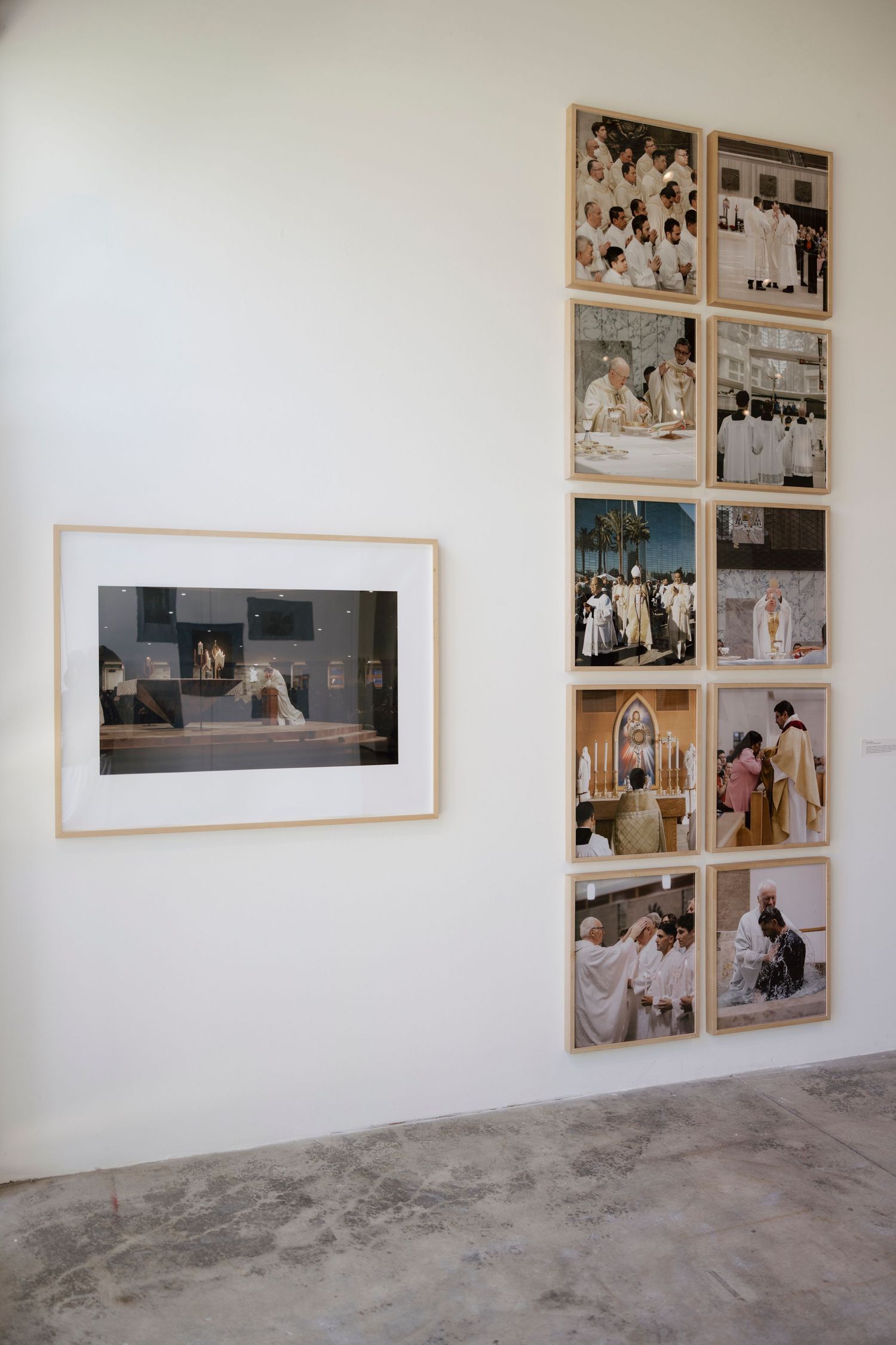 Gallery wall displaying framed religious ceremony photographs arranged in a grid alongside a single framed print on white wall.