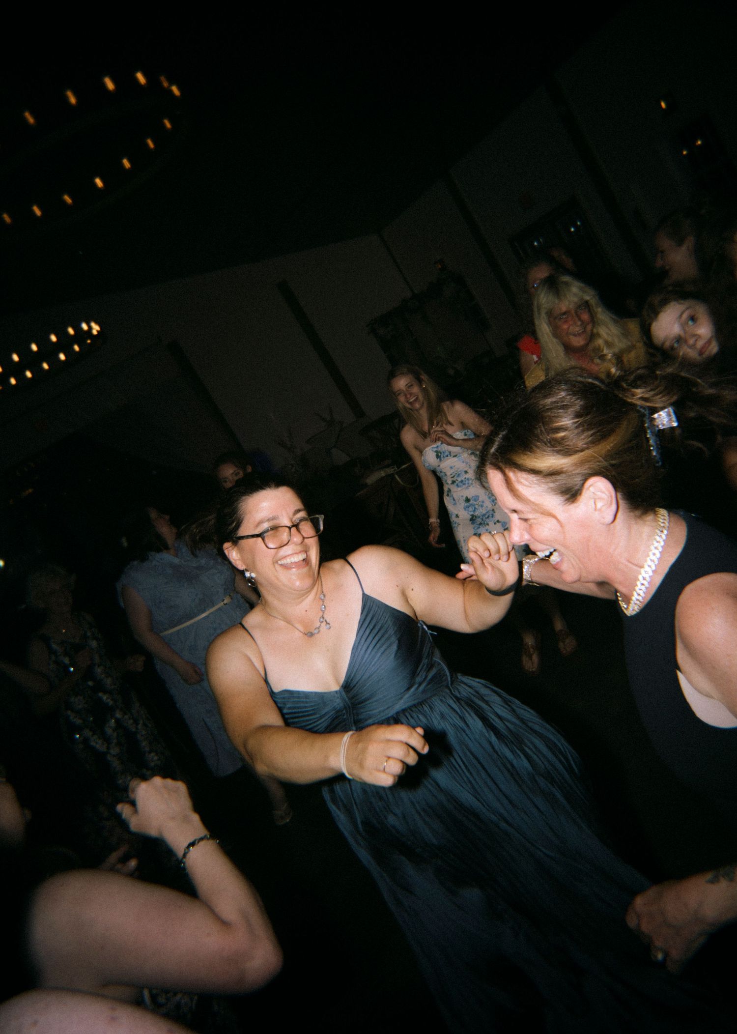 Two women laughing and dancing together at a lively indoor party event.