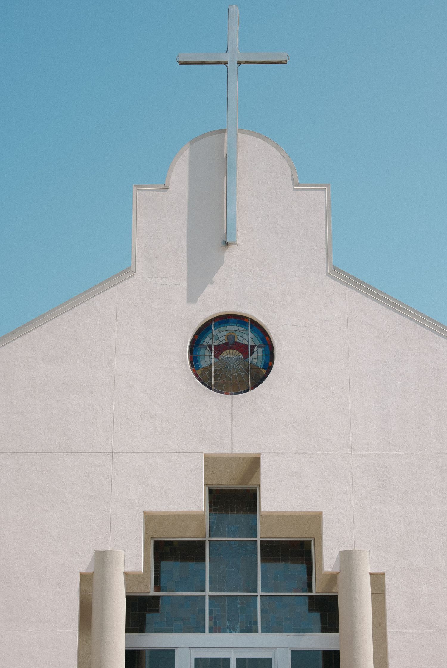 White church facade with cross and stepped architecture against blue sky.