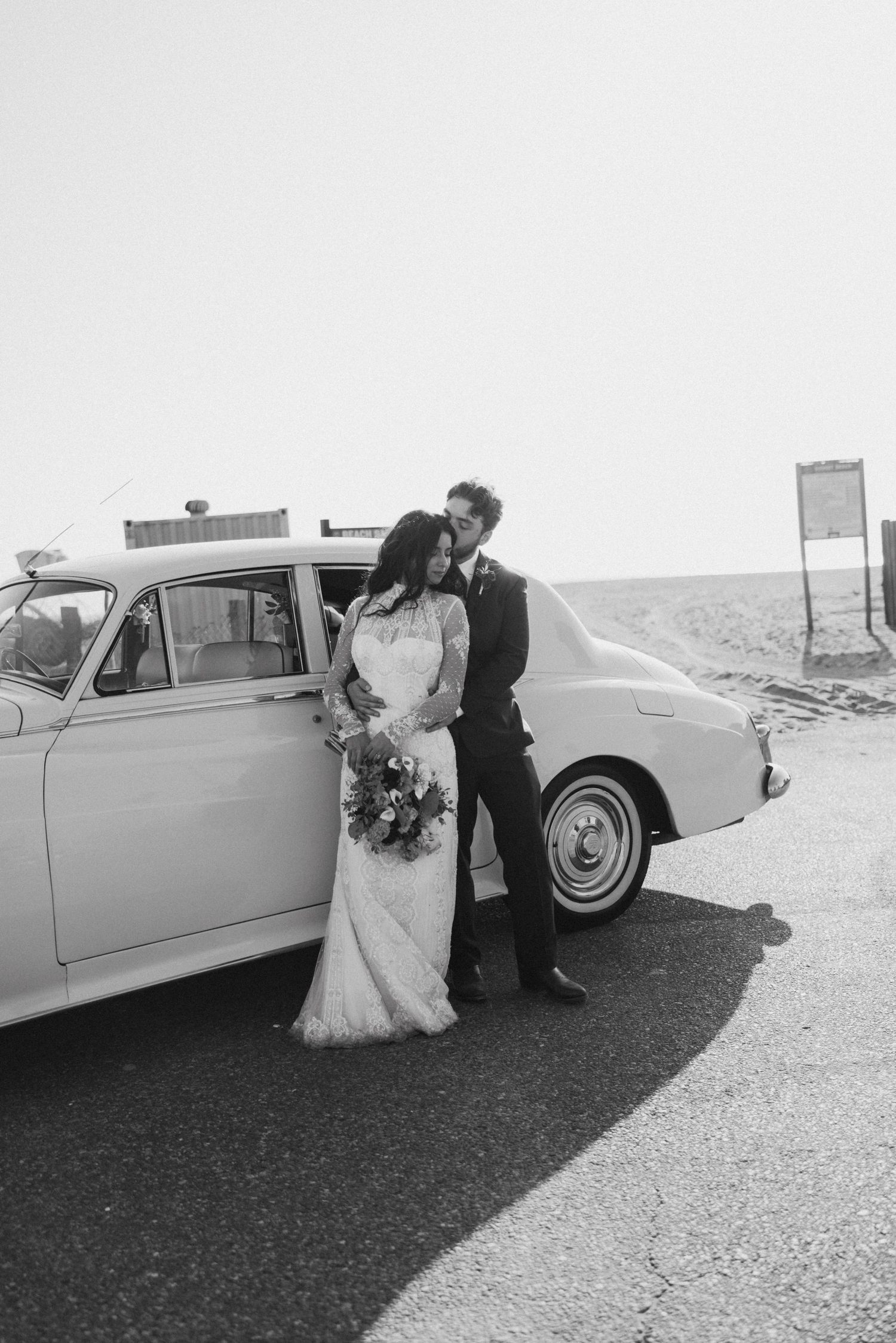 Black and white wedding portraits with a classic car on a desert road.