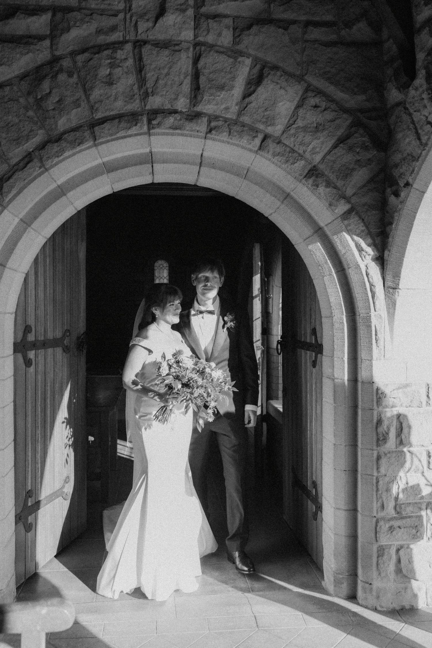 A wedding couple poses in a stone archway corridor for artistic black and white photos.
