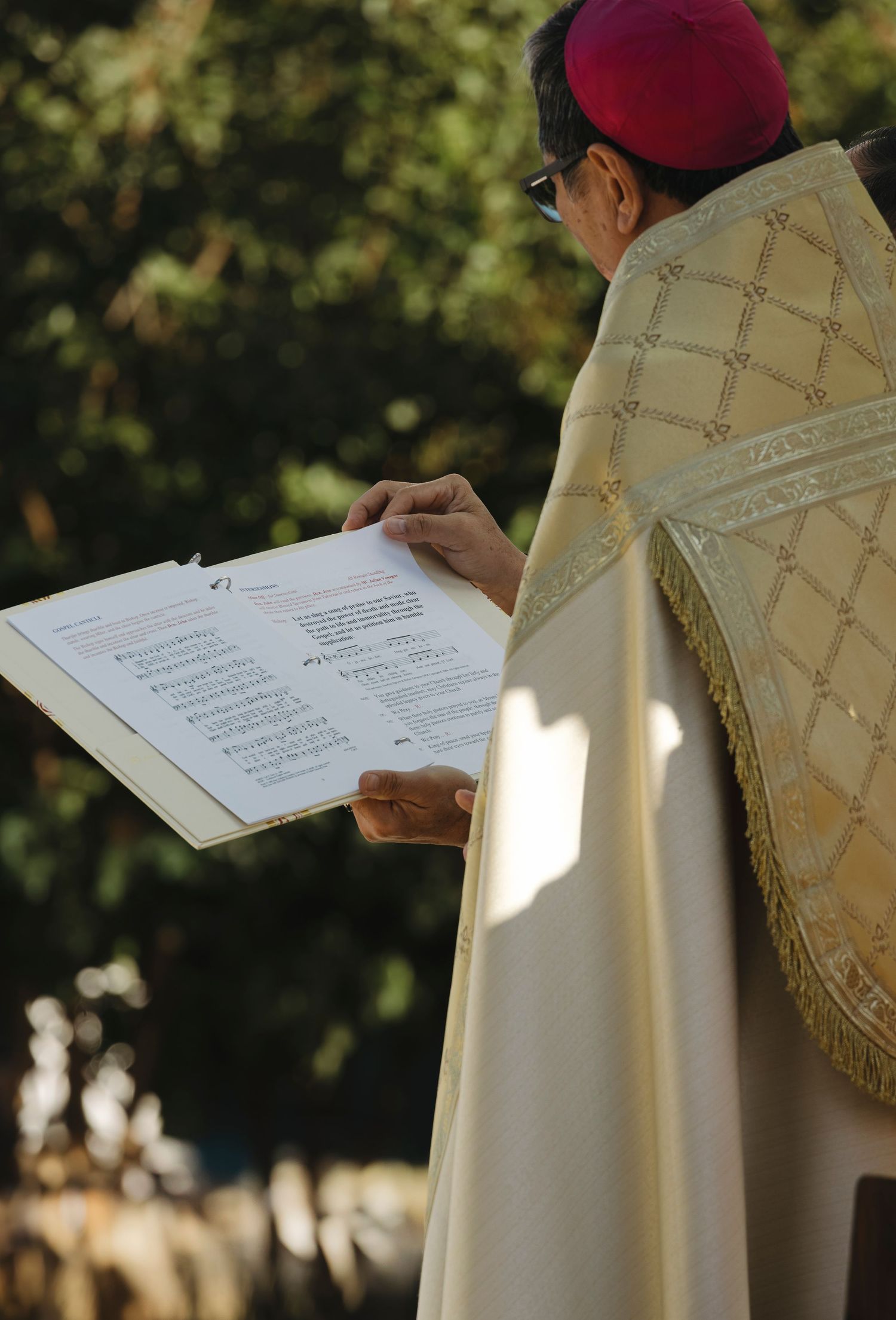 Person in ceremonial robes holding liturgical texts during an outdoor service.