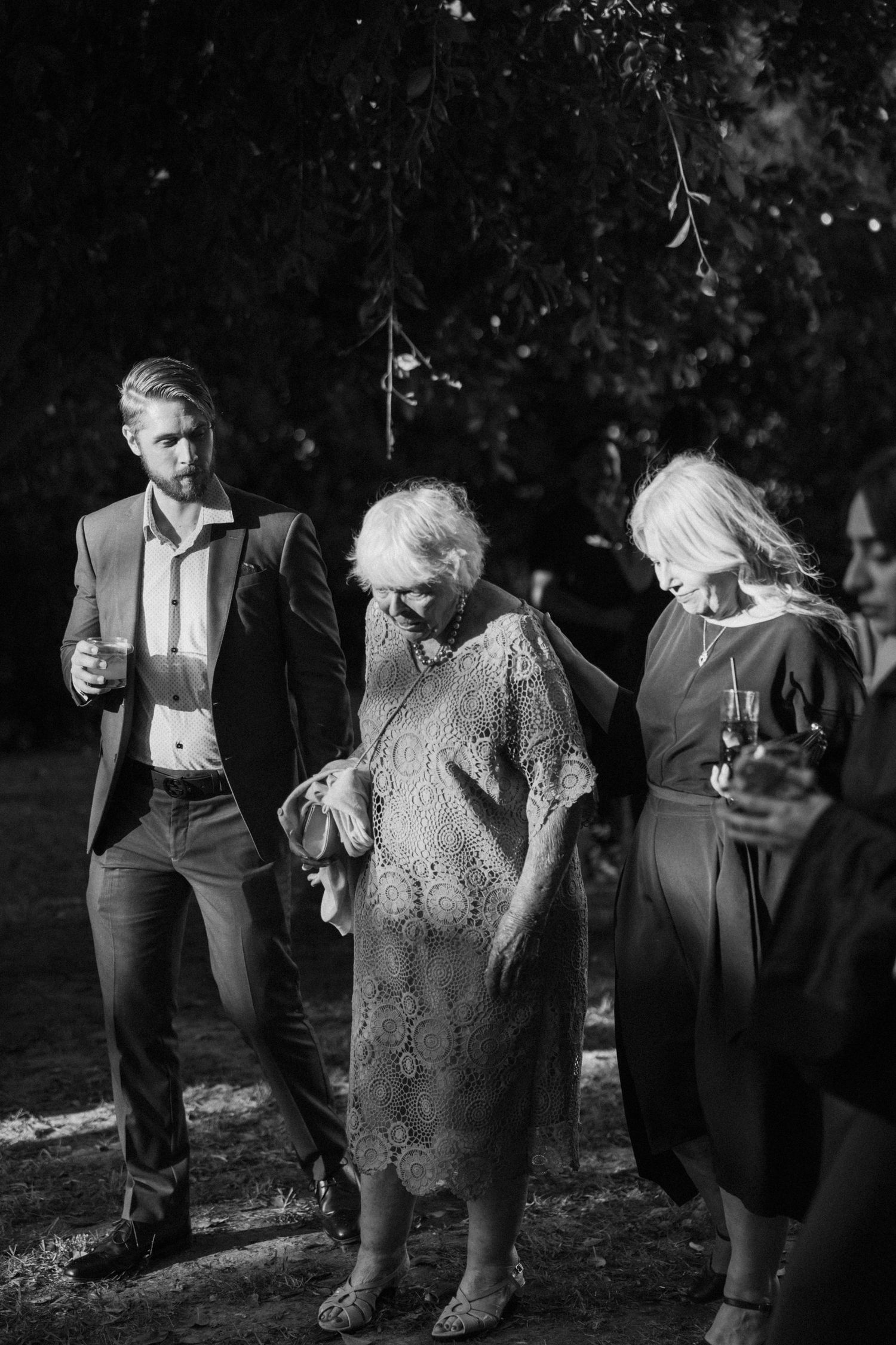 Black and white photo of wedding guests enjoying drinks and dancing at an outdoor reception.