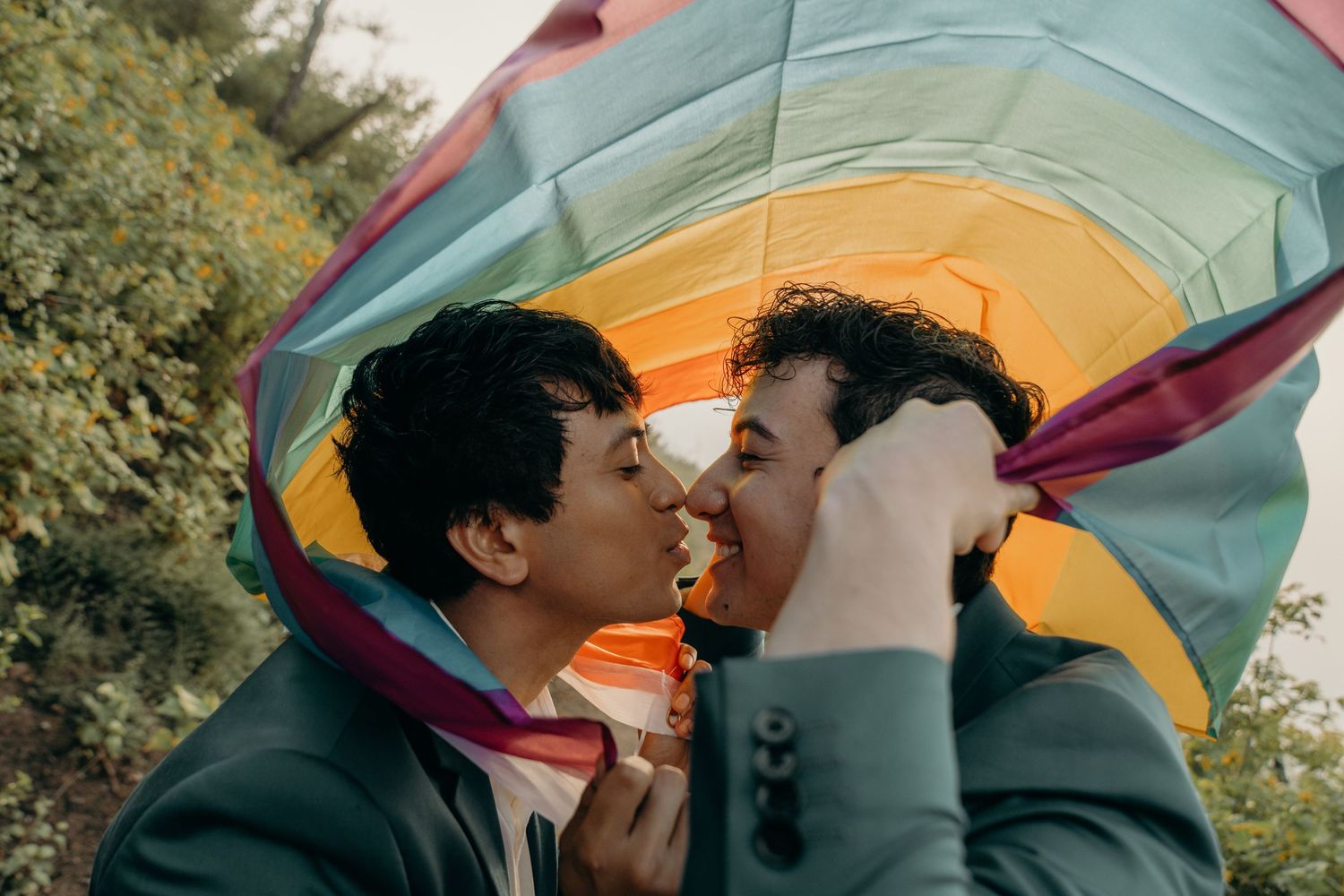 Two grooms celebrating their wedding while holding a rainbow pride flag in Malibu, California