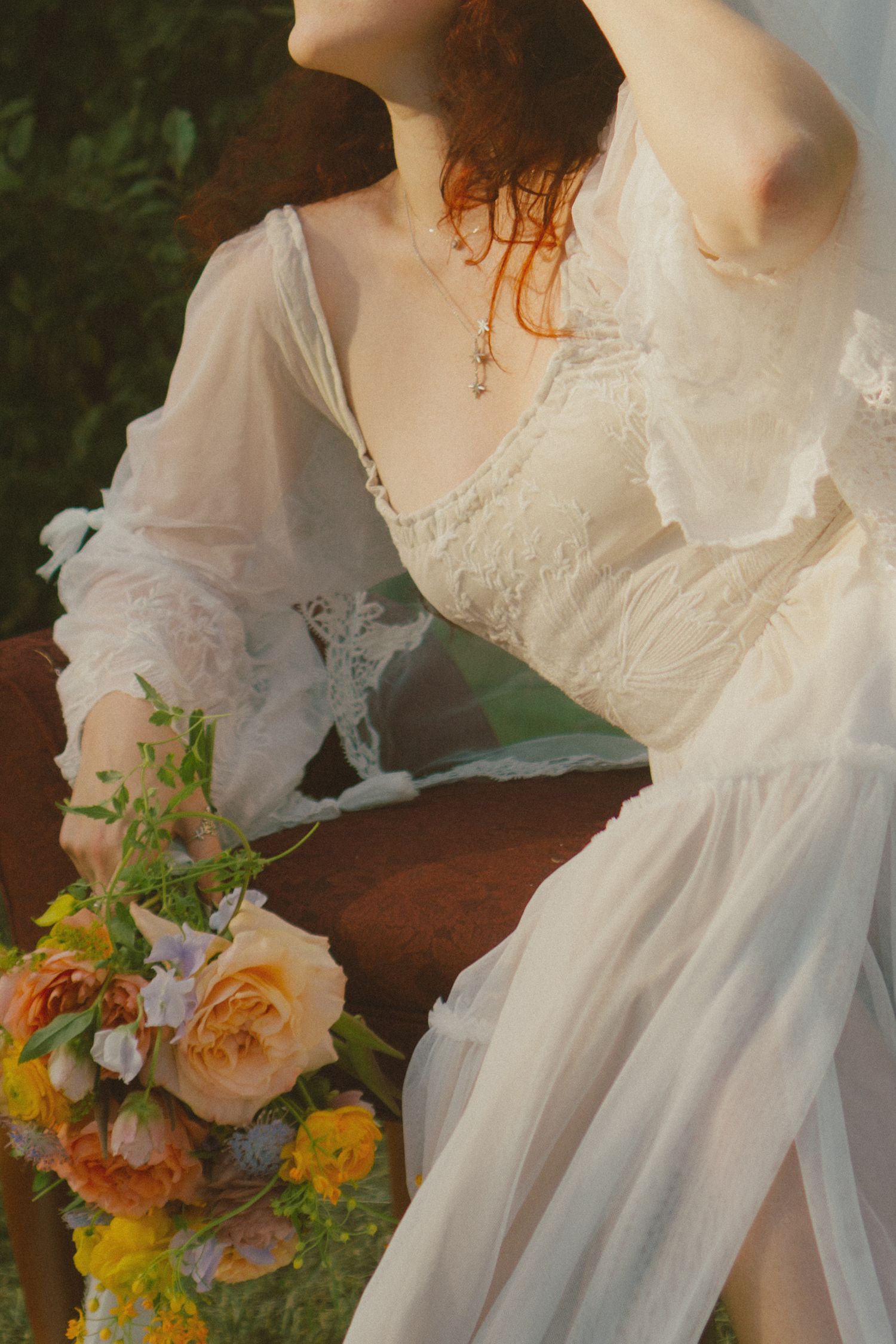 Ethereal white lace dress with sheer sleeves and orange and yellow floral bouquet in a romantic vintage style.