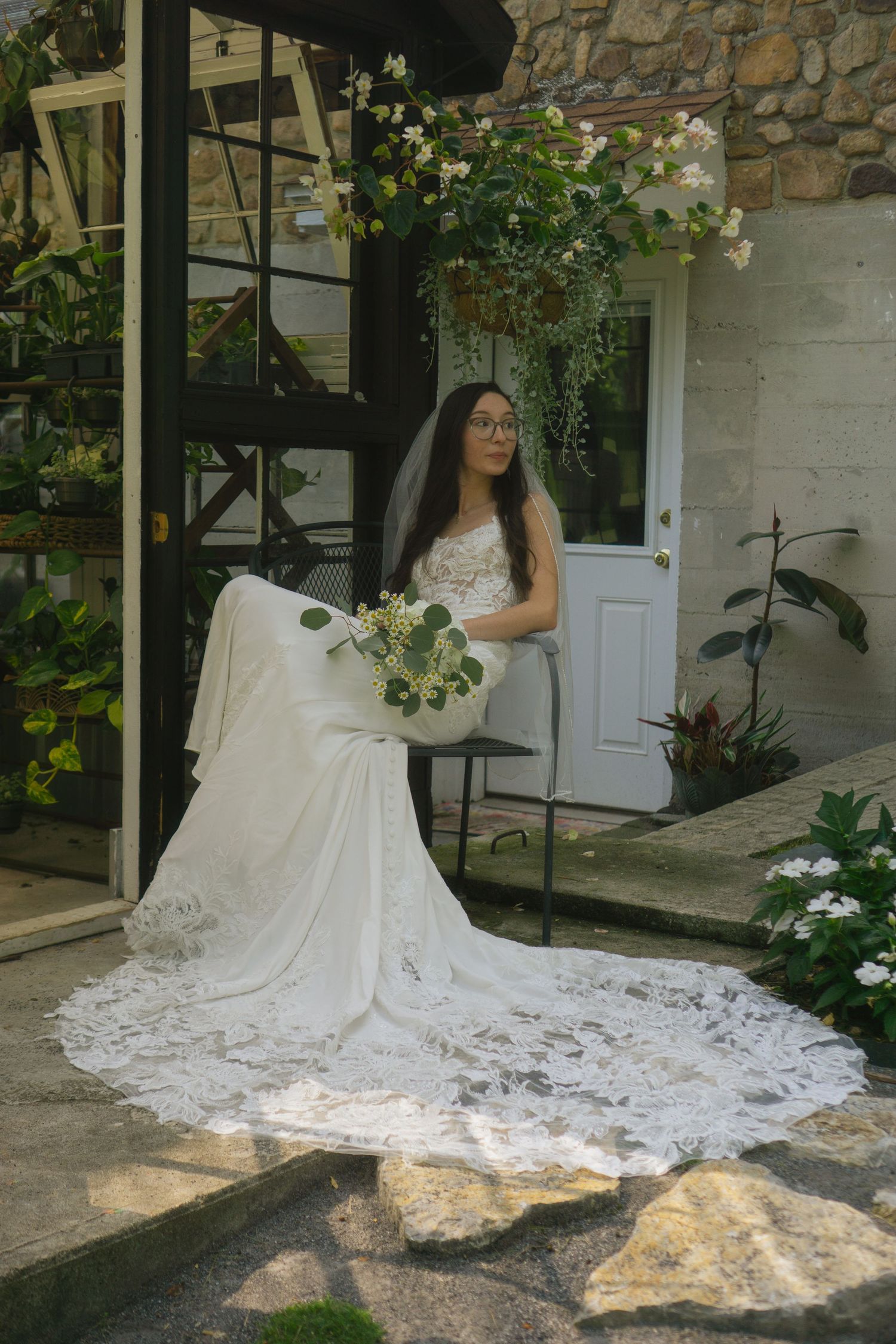 Bride in a white lace gown with long train poses elegantly against a stone wall with climbing roses.