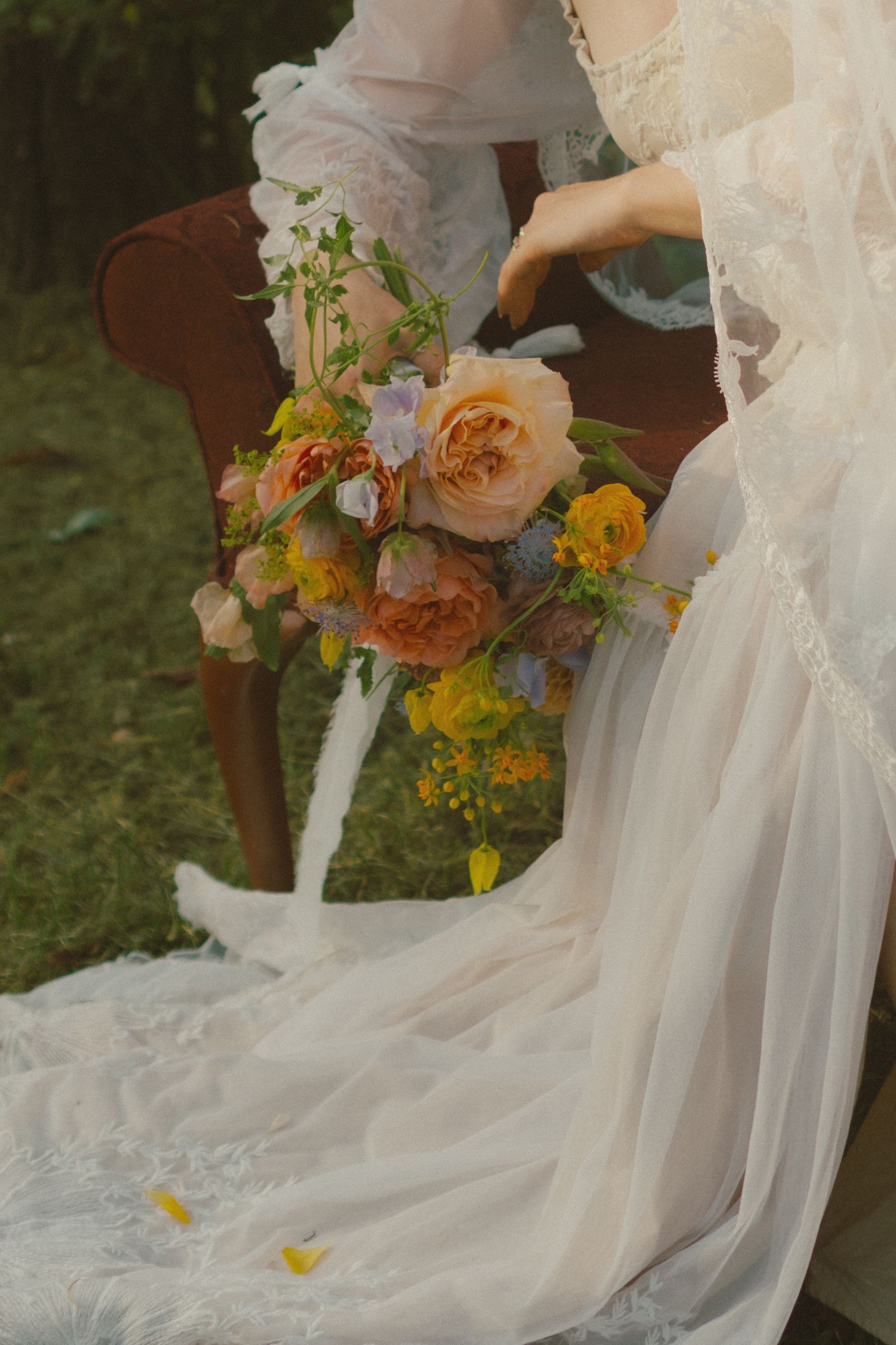 A delicate wedding bouquet with peach roses and yellow wildflowers rests against flowing white tulle fabric.