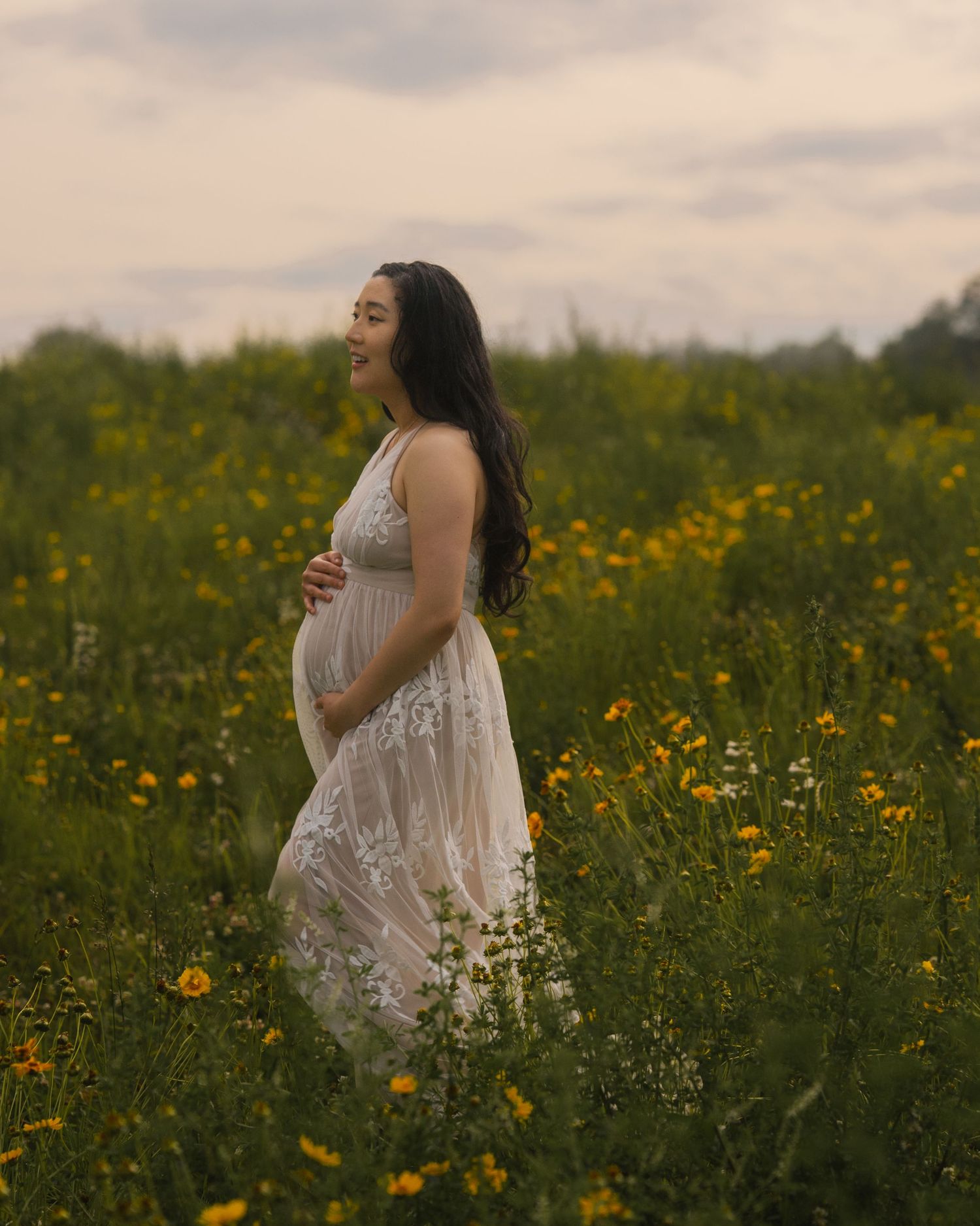A person in a white dress walks through a field of yellow wildflowers at dusk.