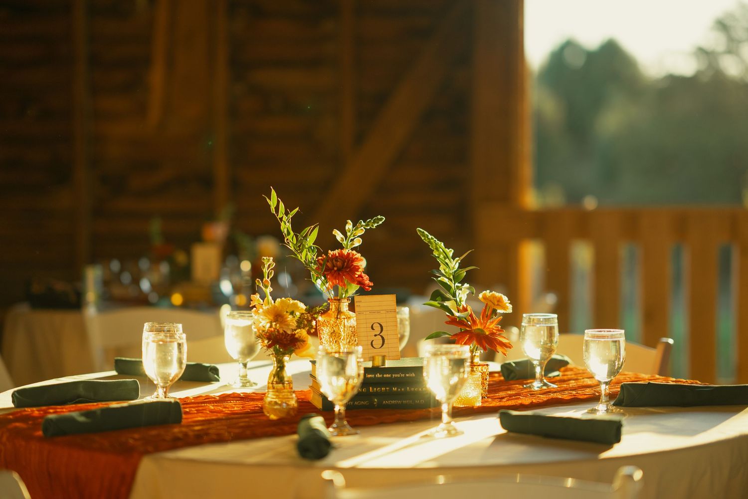 Elegant rustic table setting with floral centerpieces and warm lighting in a barn venue.