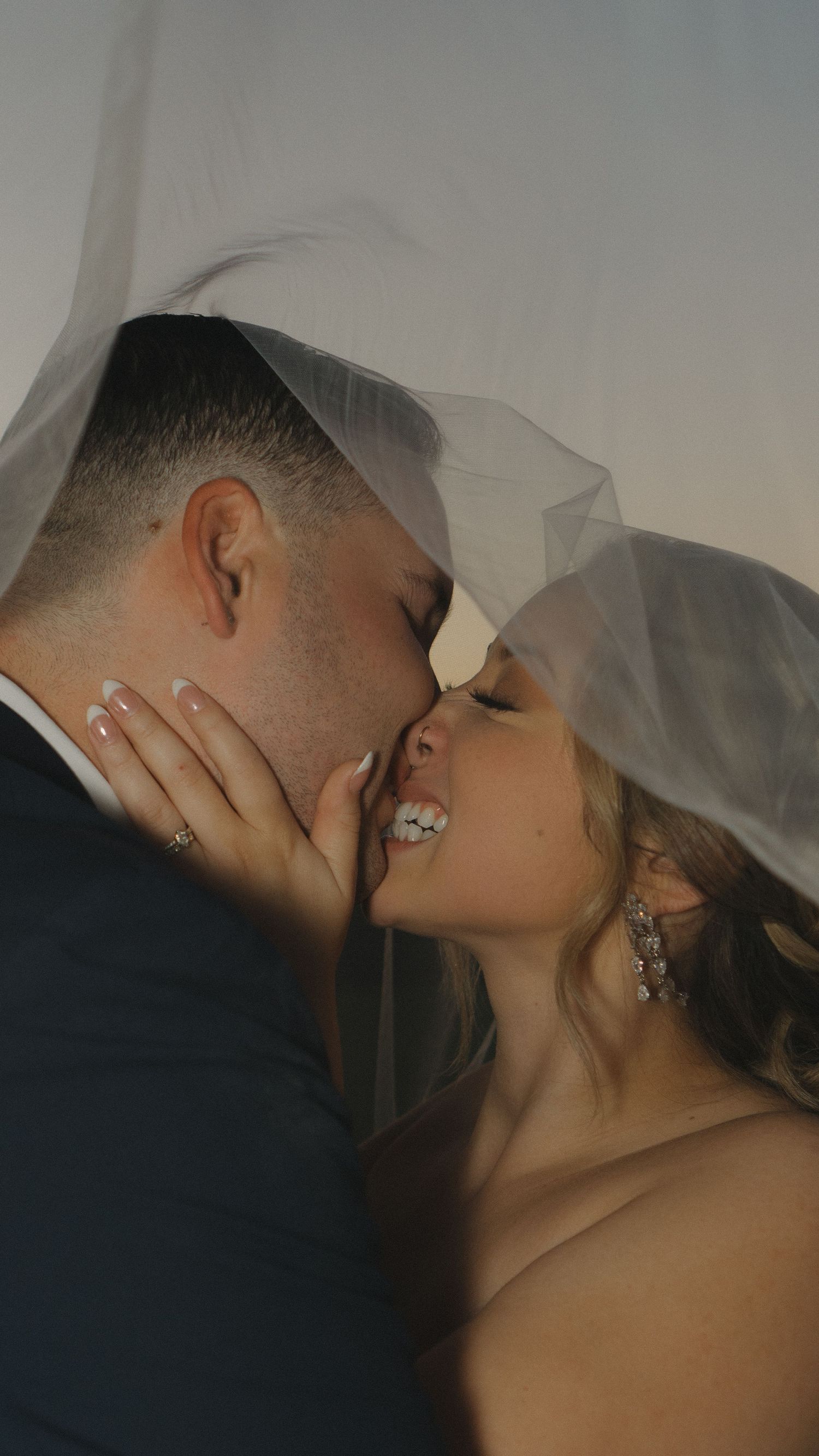A romantic wedding couple sharing an intimate kiss under a white veil in a series of artistic photographs.