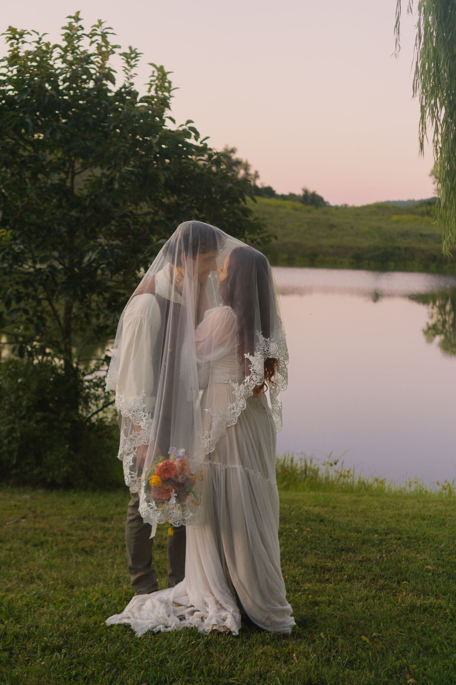 A romantic moment captured by a lake during sunset with flowing veils.