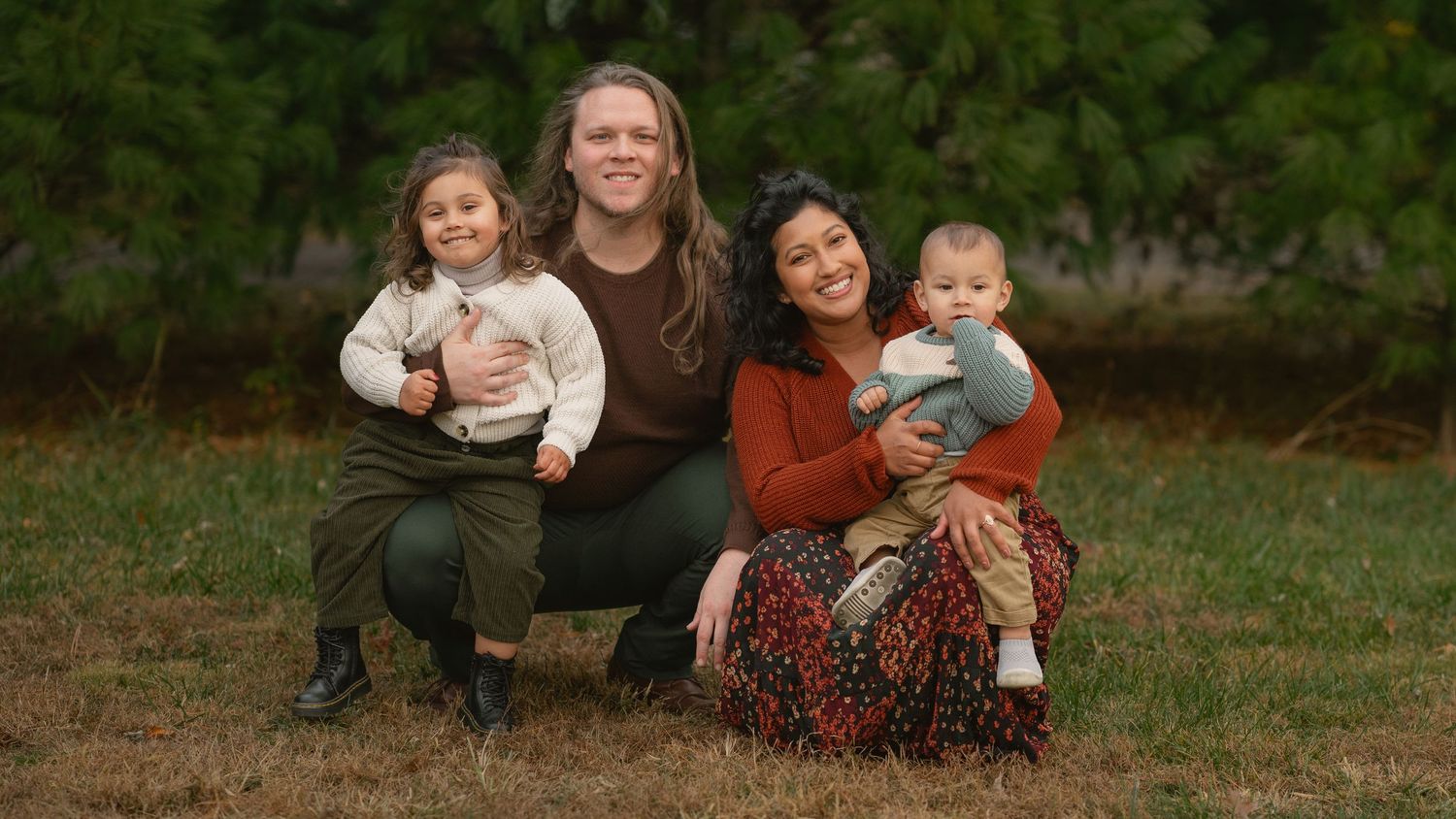 Family group sitting together on grass with evergreen trees in background. Nokesville, Virginia.