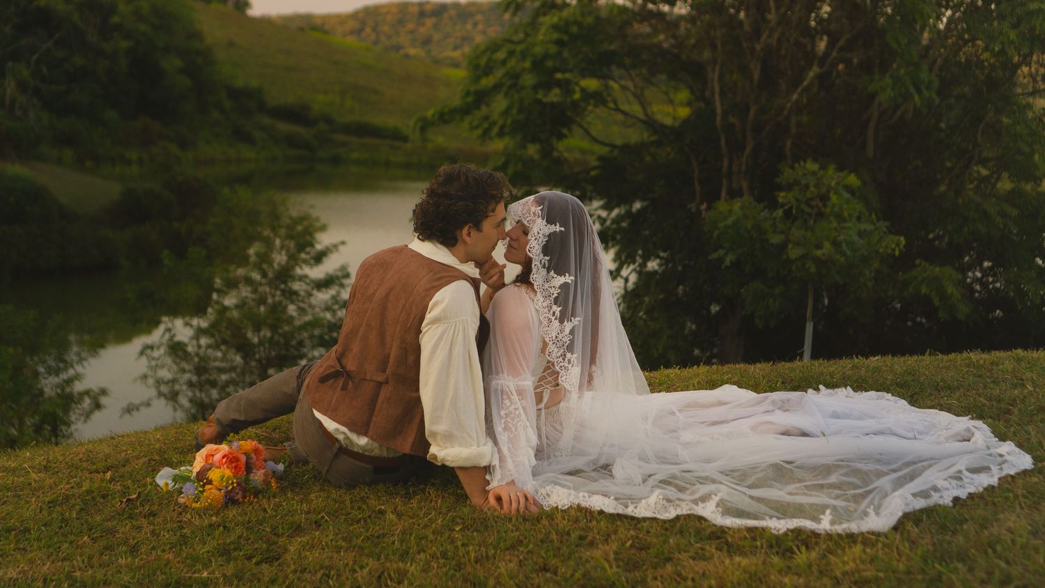 A romantic outdoor wedding scene with white flowing fabric draped between trees at sunset.