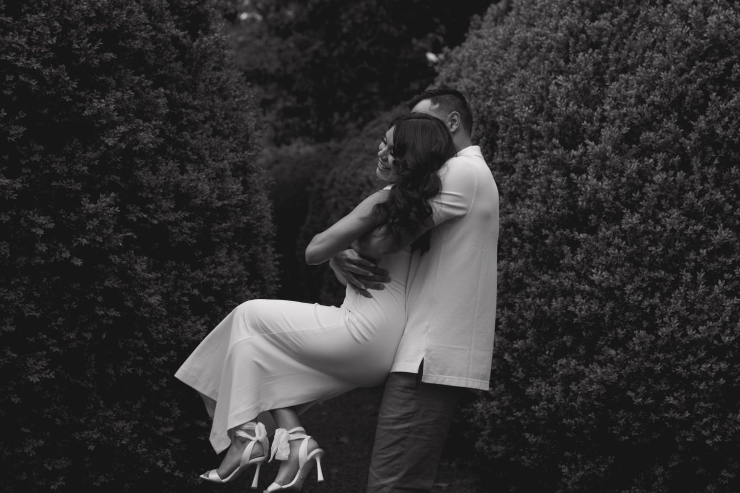 A romantic black and white photo of a couple embracing outdoors against a dark background.