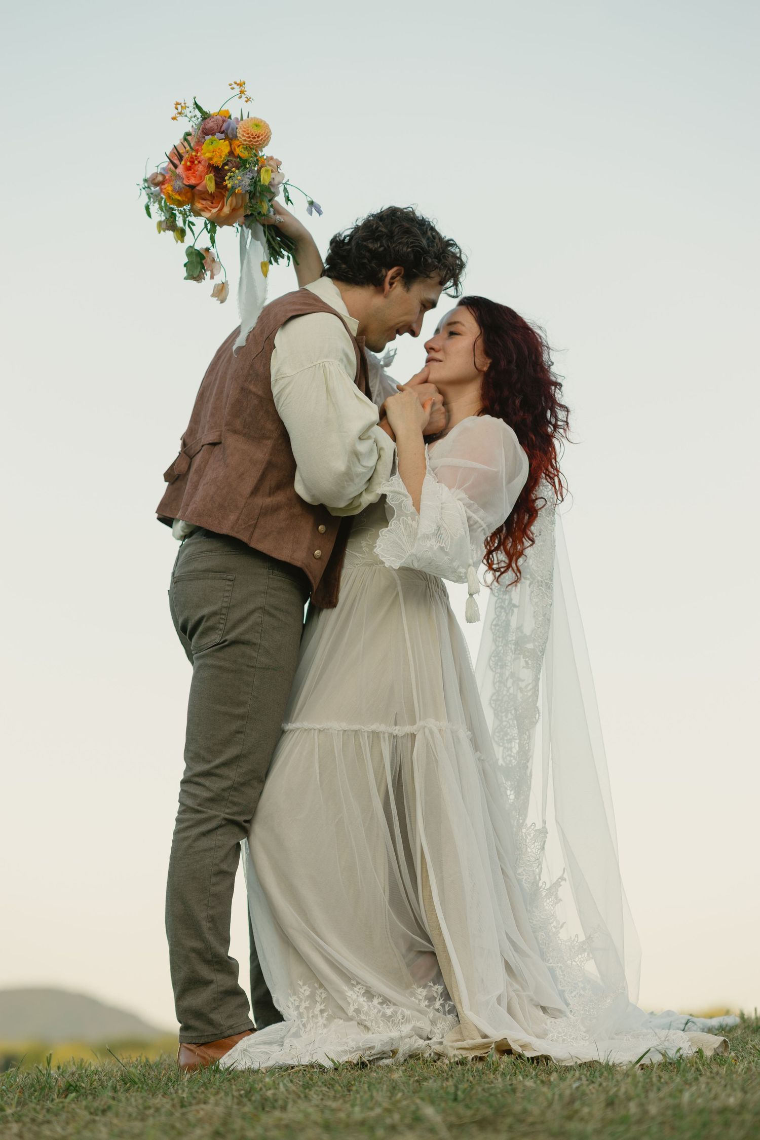 A romantic wedding couple shares a kiss in a sunlit field.