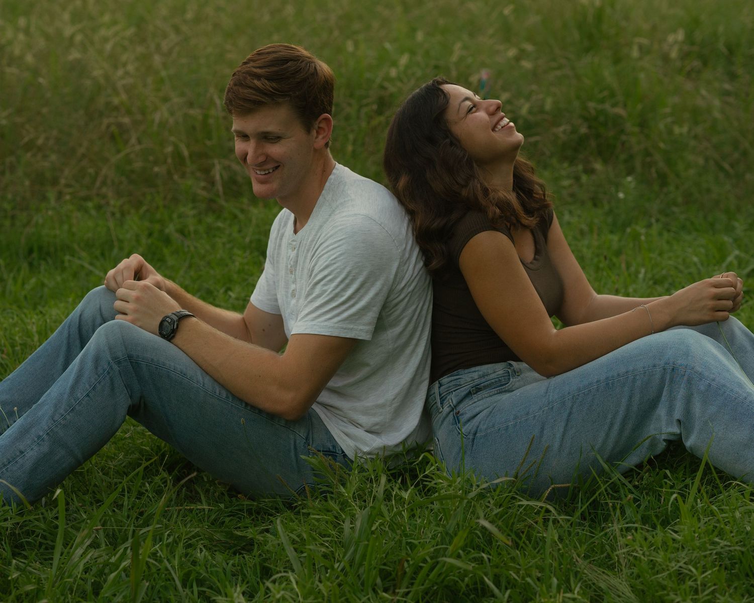 People lying in grass having candid laughs during a casual outdoor photoshoot.