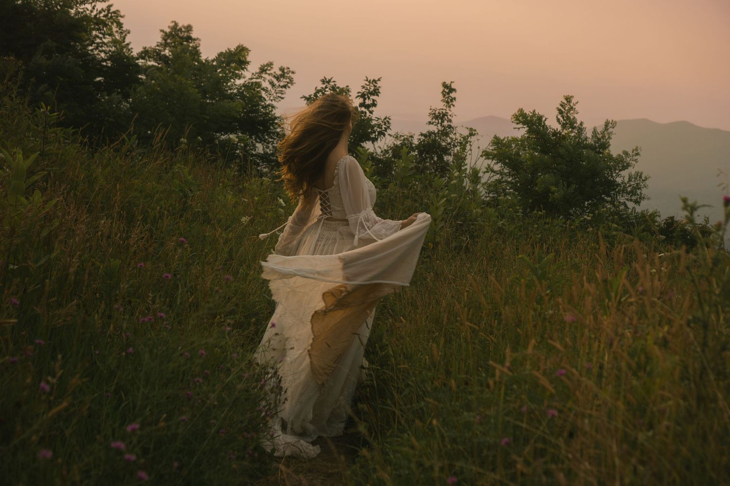 a woman frolicking in a field of tall grass and wildflowers with a breathtaking view of the Shenandoah Mountains in Virginia