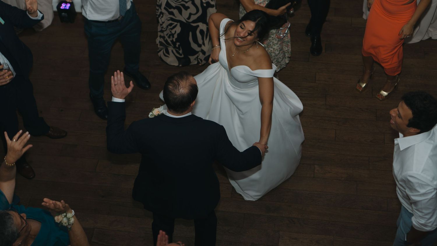 People dancing and celebrating on a dark wooden dance floor at a party or event.