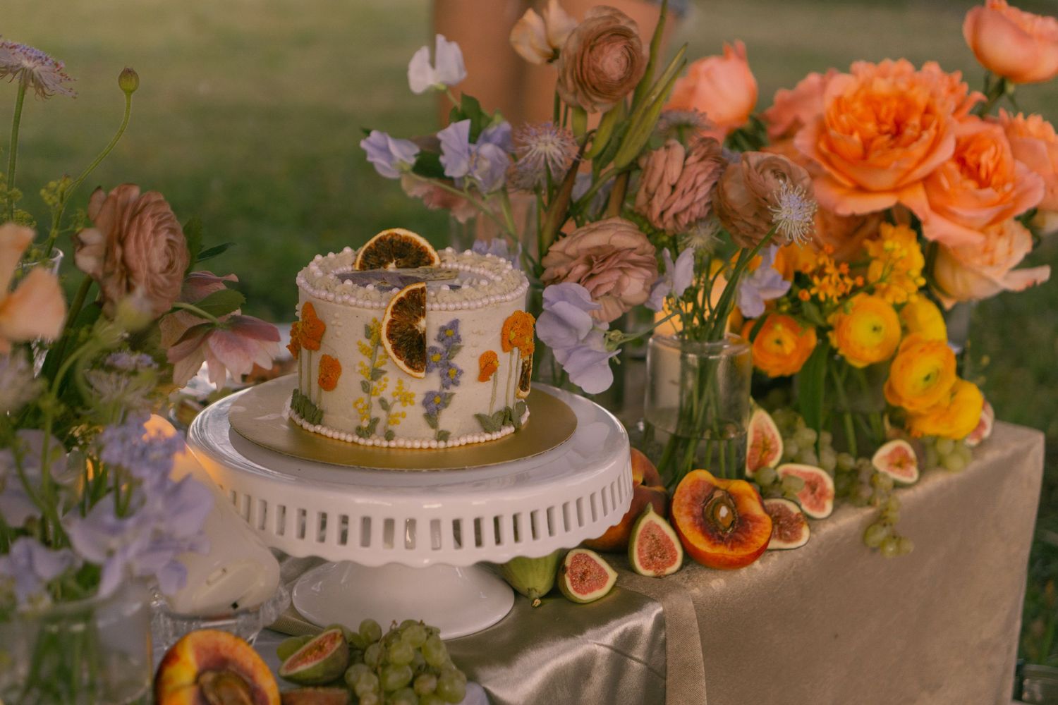 Wedding dessert table decorated with orange flowers and a white tiered cake.