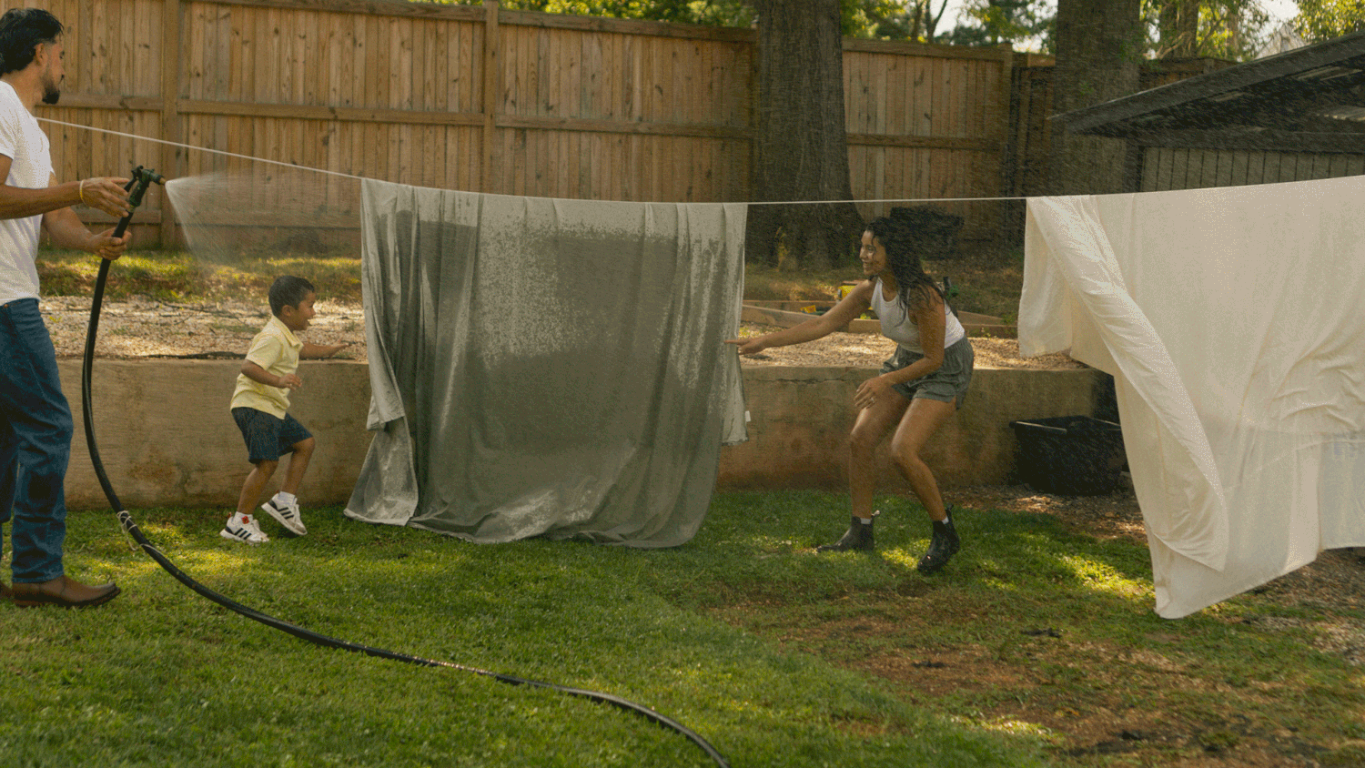 a family in a backyard setting playing with the water hose and running around